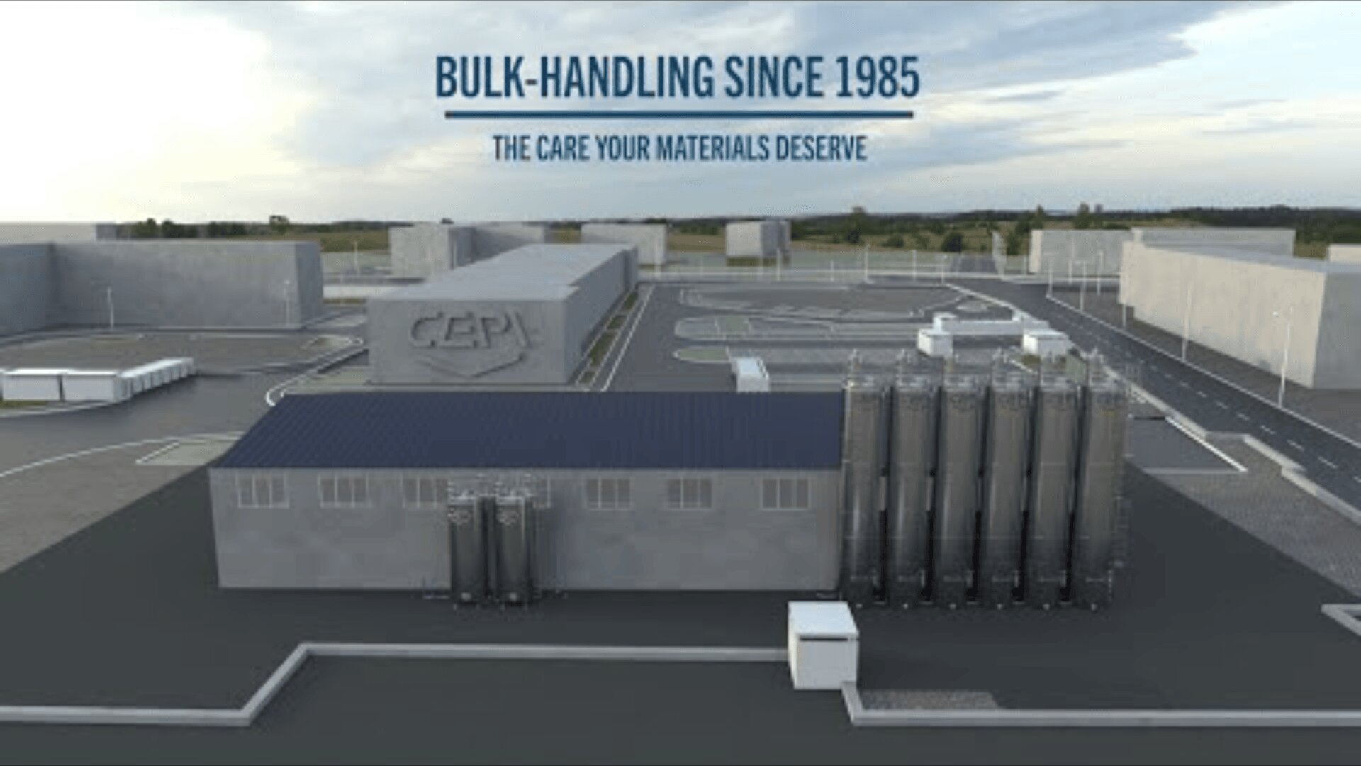 A modern industrial facility with silos and large buildings, featuring the text BULK-HANDLING SINCE 1985 and THE CARE YOUR MATERIALS DESERVE above the complex. The scene is set under a cloudy sky.