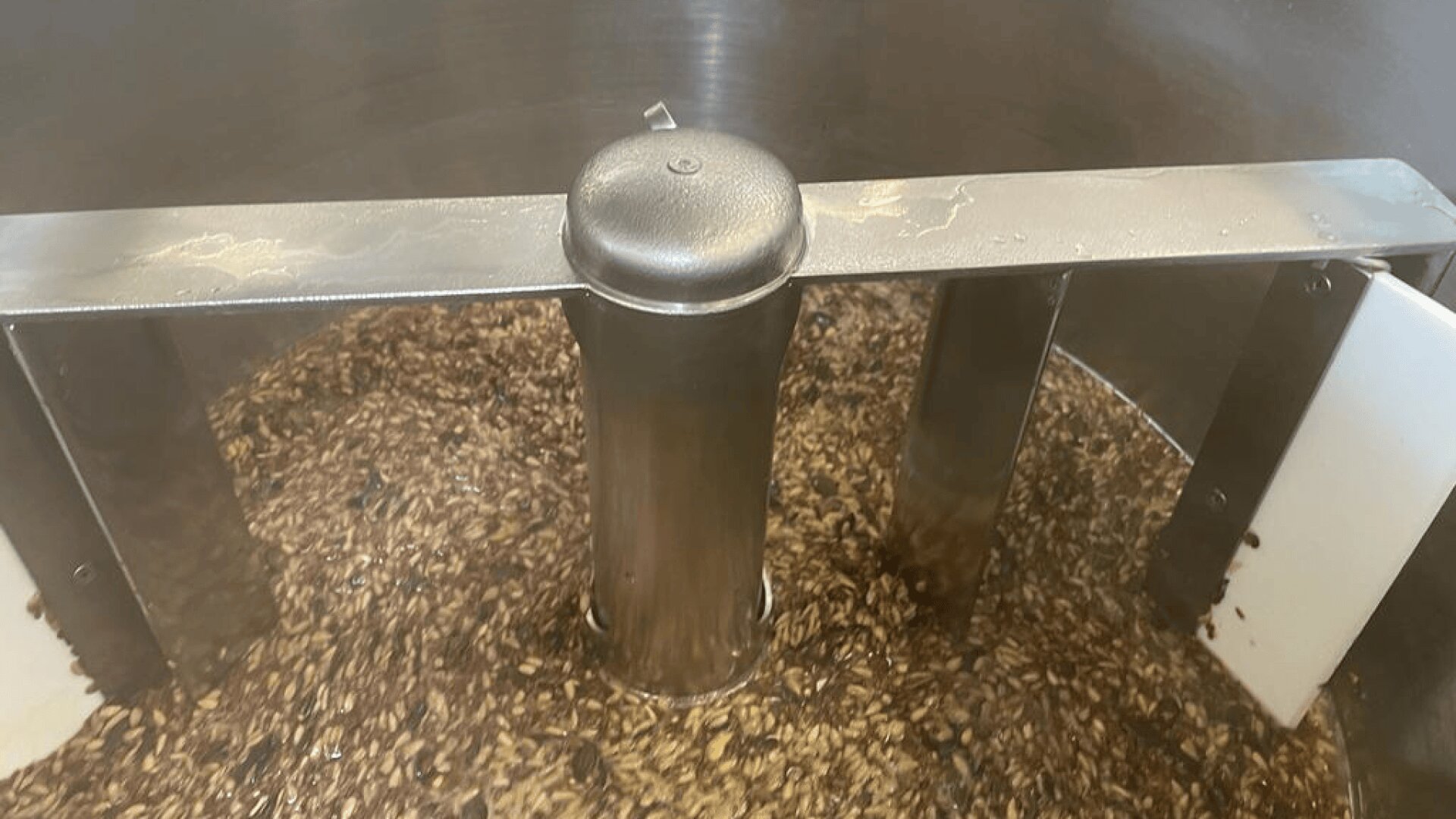 Nahaufnahme eines Braukessels mit einem Metallrührwerk, das ein Gemisch aus Getreide und Flüssigkeit während des Maischprozesses bei der Bierherstellung umrührt.