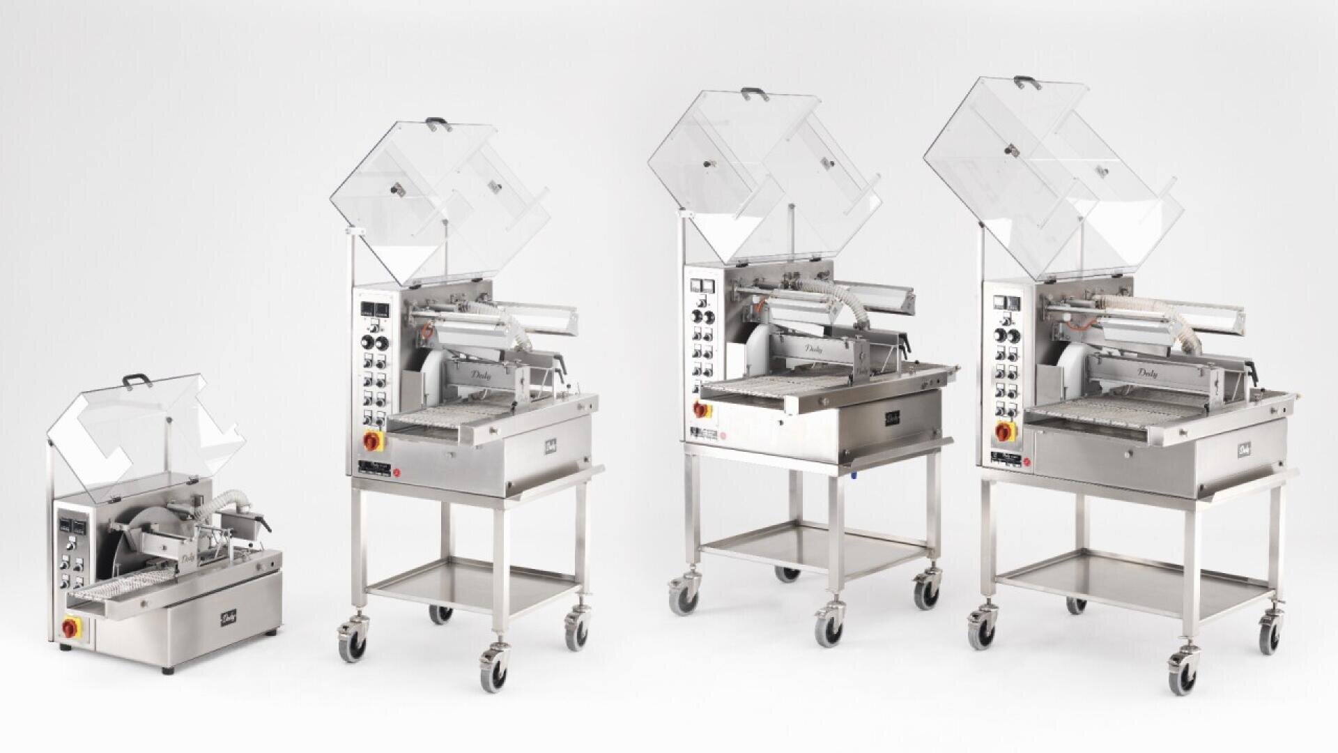 Four stainless steel industrial vacuum packaging machines of varying sizes are displayed in a row on white background, each with transparent lids open and control panels visible on the front.