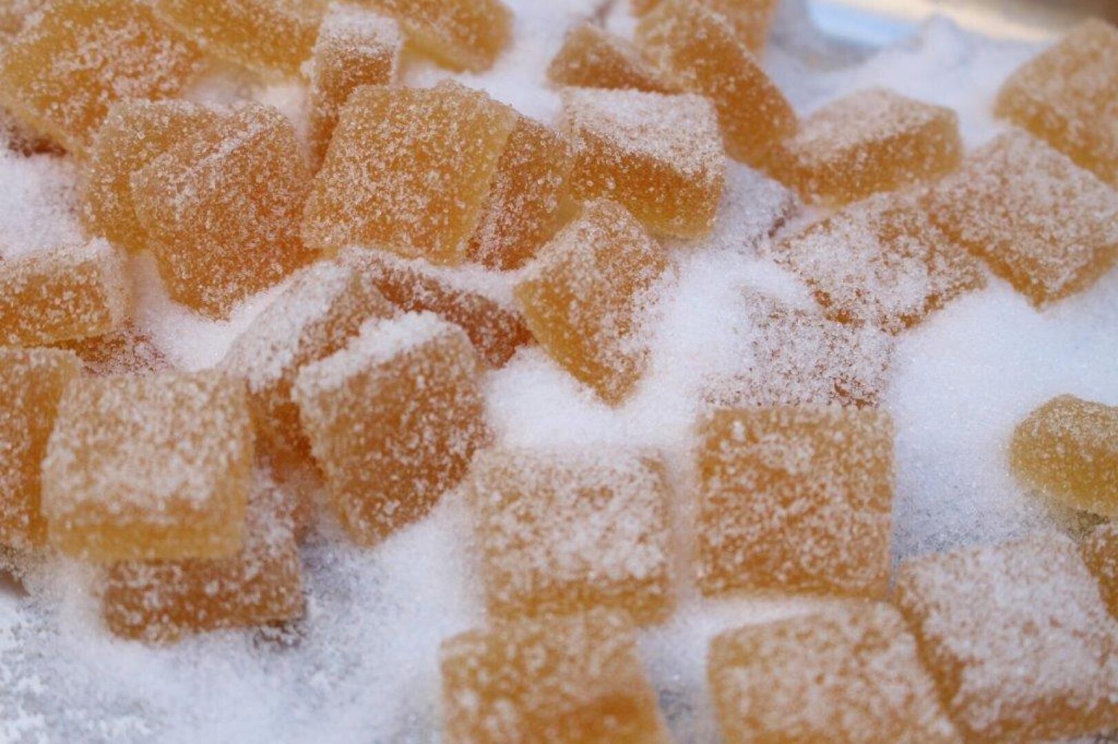 Nahaufnahme von goldbraunen, mit Zucker überzogenen Gummibonbonquadraten, die auf einer mit Kristallzucker bedeckten Fläche verstreut sind.