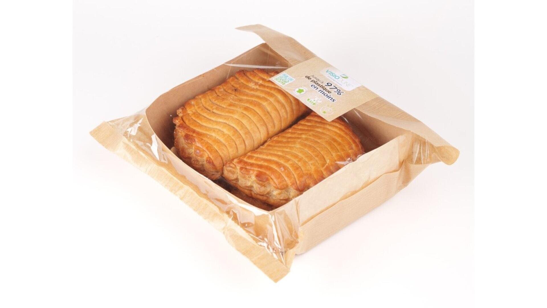 Zwei goldbraune Blätterteigtaschen sind in einer teilweise geöffneten braunen Papierschachtel mit einem durchsichtigen Kunststofffenster verpackt, in dem das Gebäck vor einem schlichten weißen Hintergrund zu sehen ist.