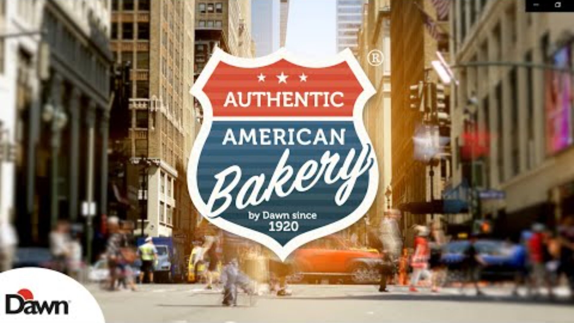 A busy city street scene is blurred in the background. In the foreground, a shield-shaped sign reads Authentic American Bakery by Dawn since 1920 with red, white, and blue colors. The Dawn logo appears in the corner.