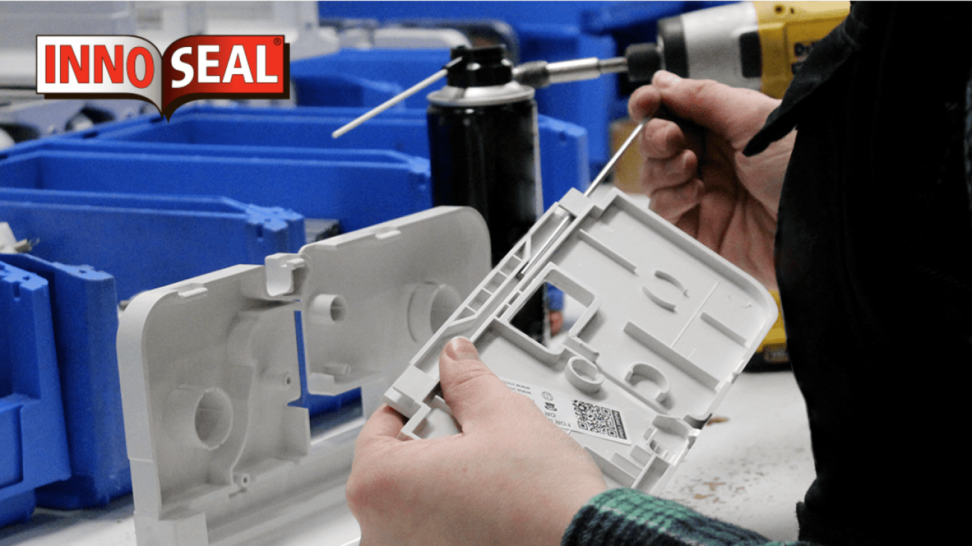 Eine Person reinigt ein weißes Kunststoffgeräteteil mit einem Wattestäbchen an einem Arbeitsplatz mit blauen Lagerbehältern. Das Innoseal-Logo ist in der oberen linken Ecke zu sehen.