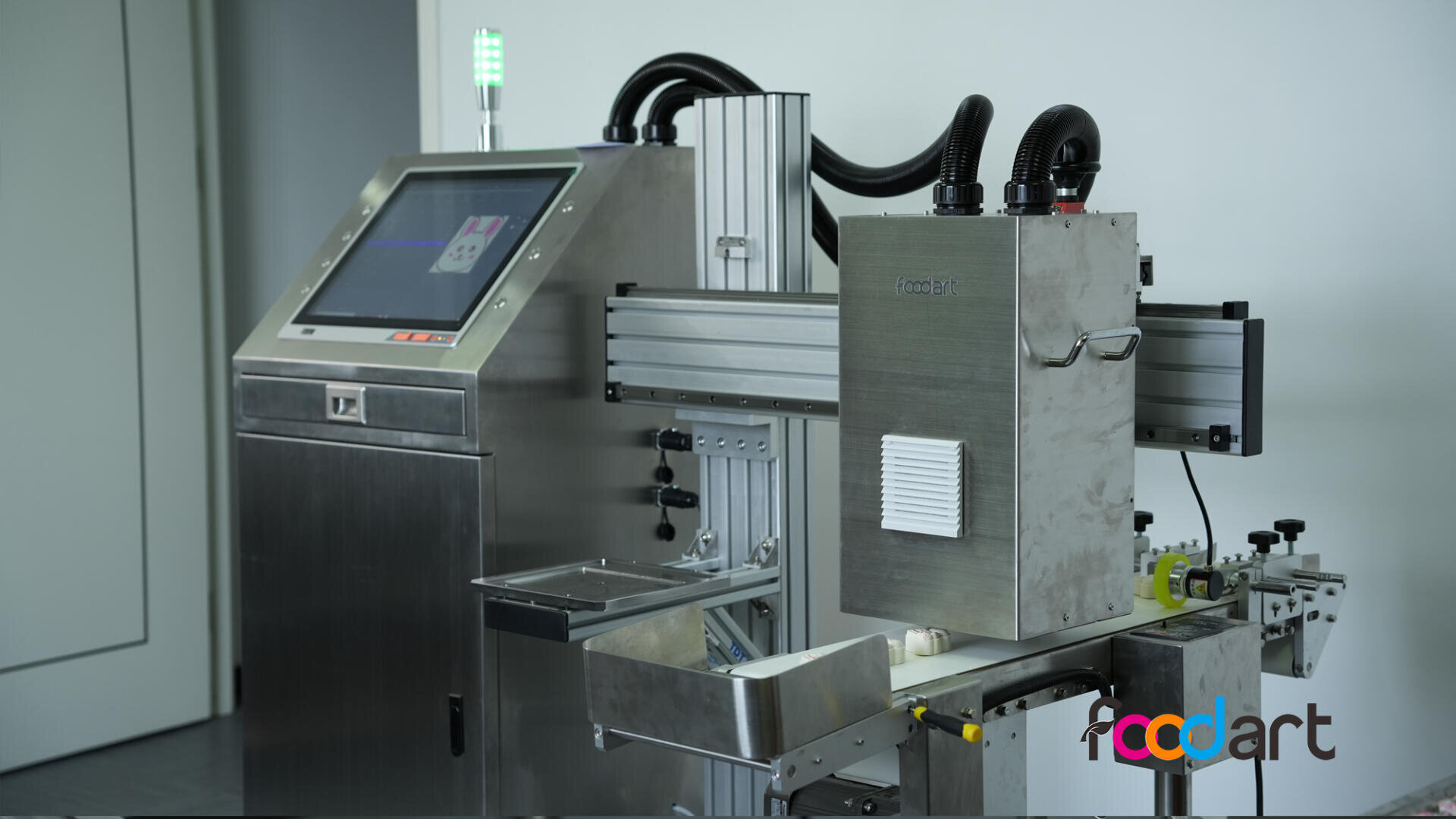 A stainless steel food processing machine with a touchscreen interface and conveyor system, featuring the foodart logo in colorful letters on the front panel.