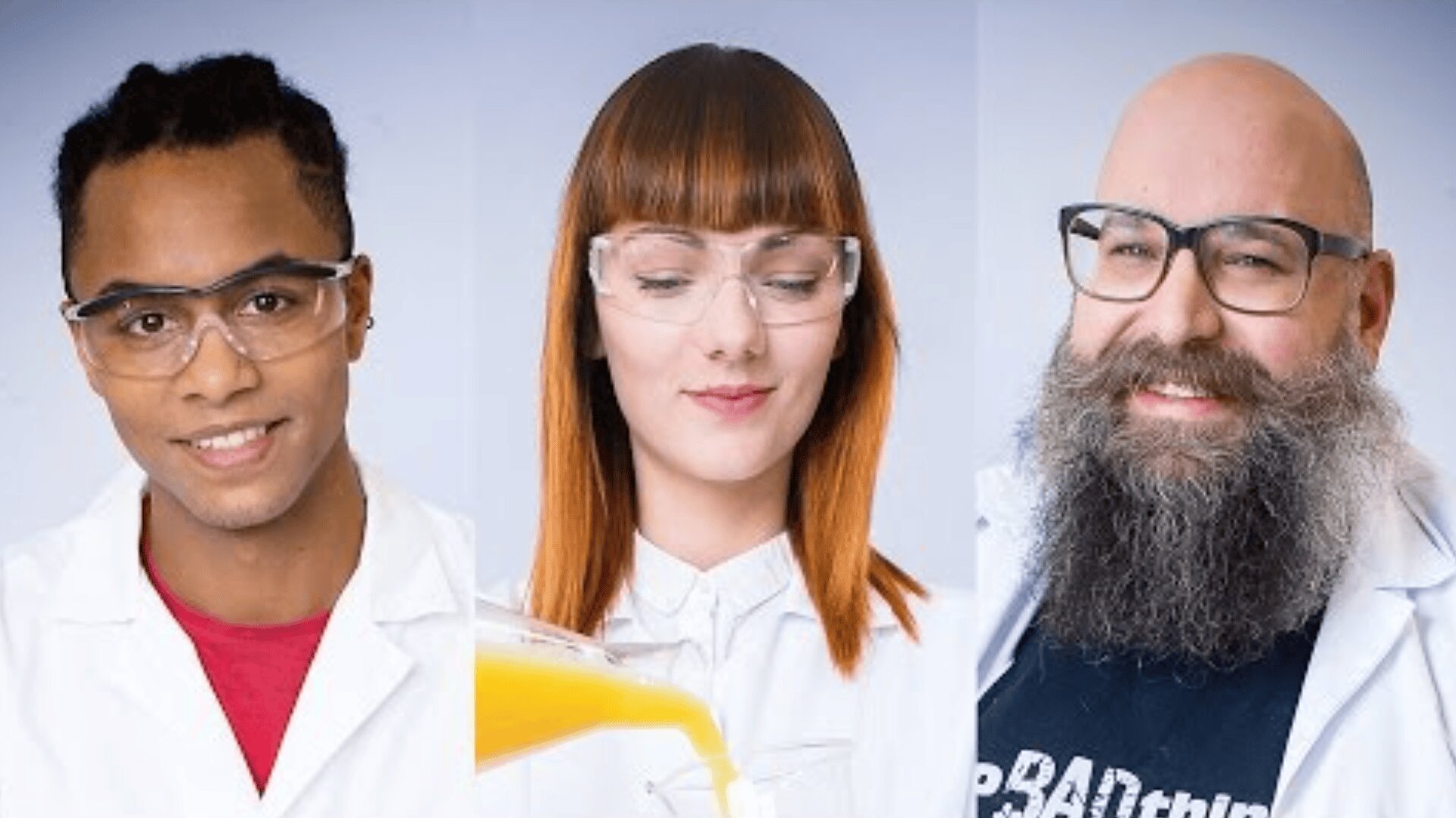 Three scientists in lab coats and safety glasses: a smiling man with dark braids, a woman with straight red hair pouring orange liquid, and a bearded man with glasses, all against a light background.