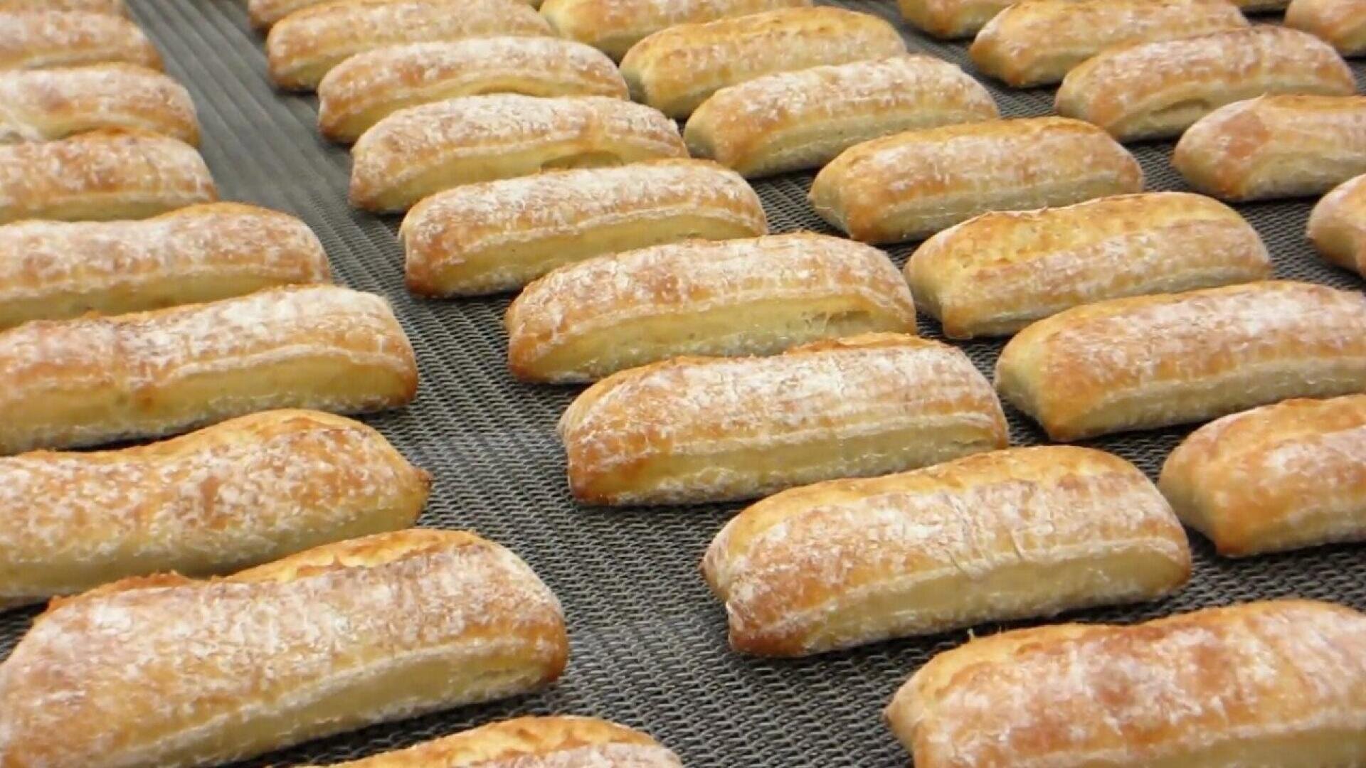 Reihen von gleichmäßig verteilten, goldbraunen, mit Puderzucker bestäubten Backwaren liegen auf einem Förderband, wahrscheinlich in einer Großbäckerei.