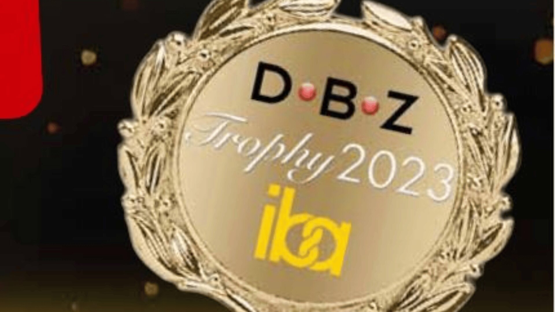 Eine goldene Lorbeerkranzmedaille zeigt den Text: D.B.Z.-Trophäe 2023 iba vor einem dunklen Hintergrund mit kleinen hellen Flecken.