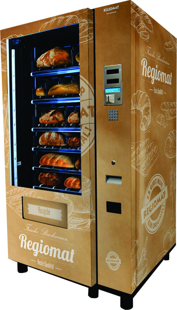Ein blauer Verkaufsautomat mit der Aufschrift Regiomat mit durchsichtigen Fächern, in denen sich mehrere Brote befinden, und einem Tastenfeld, einem Münzeinwurf und einem Bildschirm auf der Vorderseite.