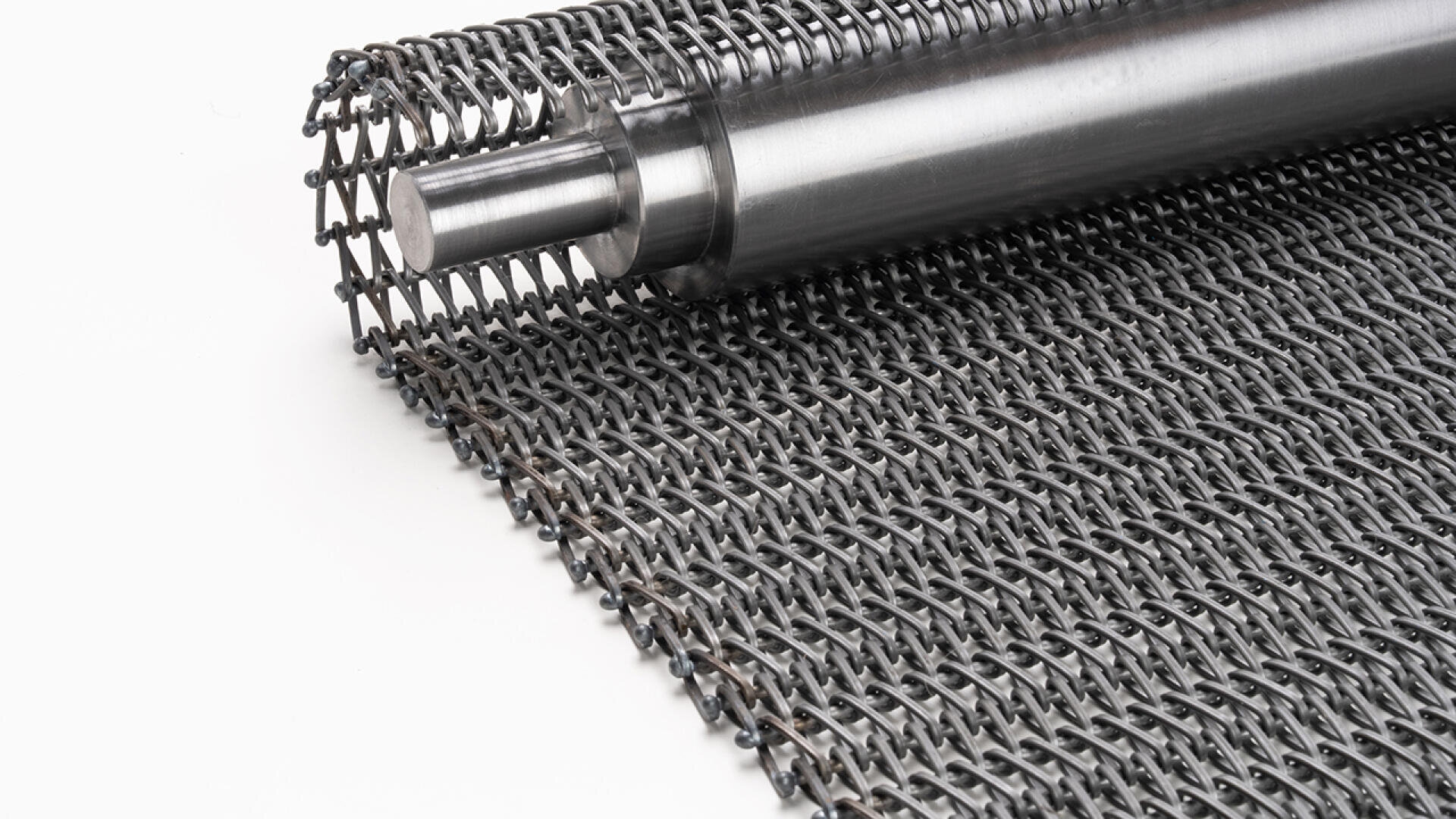 Eine Nahaufnahme eines Förderbands aus gerolltem Metall mit ineinandergreifendem Drahtgeflecht und einer zylindrischen Metallstange an einem Ende, auf einem weißen Hintergrund platziert.
