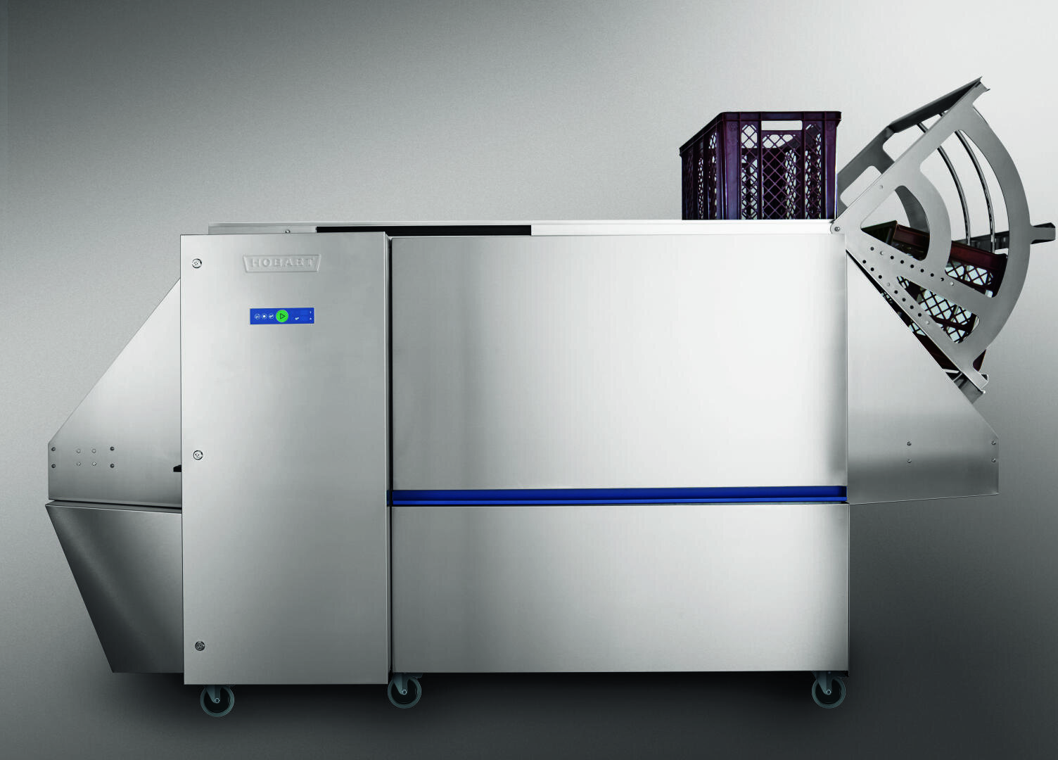A large, stainless steel industrial dishwasher with a wheeled base, a control panel, and a crate of dishes loading into the open circular hatch on the right side.