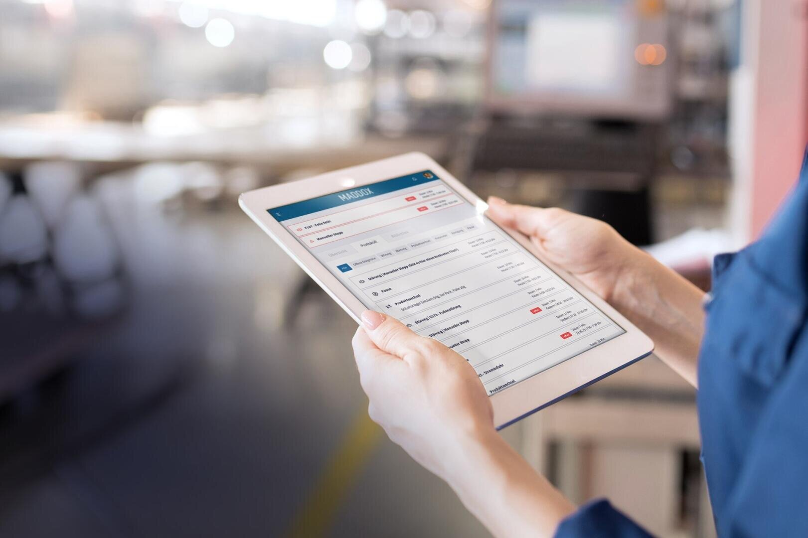 Eine Person hält in einer hellen, modernen Büroumgebung ein Tablet mit einer Projektmanagement- oder Aufgabenverfolgungsanwendung, auf deren Bildschirm Aufgabenlisten, Termine und Status angezeigt werden.