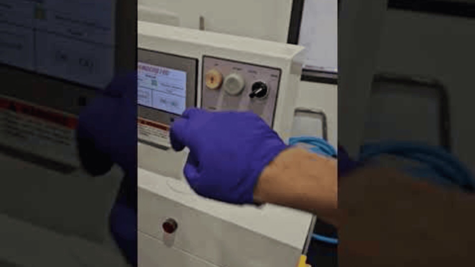 Eine Person, die einen lila Handschuh trägt, bedient ein Bedienfeld an einer Maschine und drückt auf einen Touchscreen mit sichtbaren Ziffernblättern und Tasten.