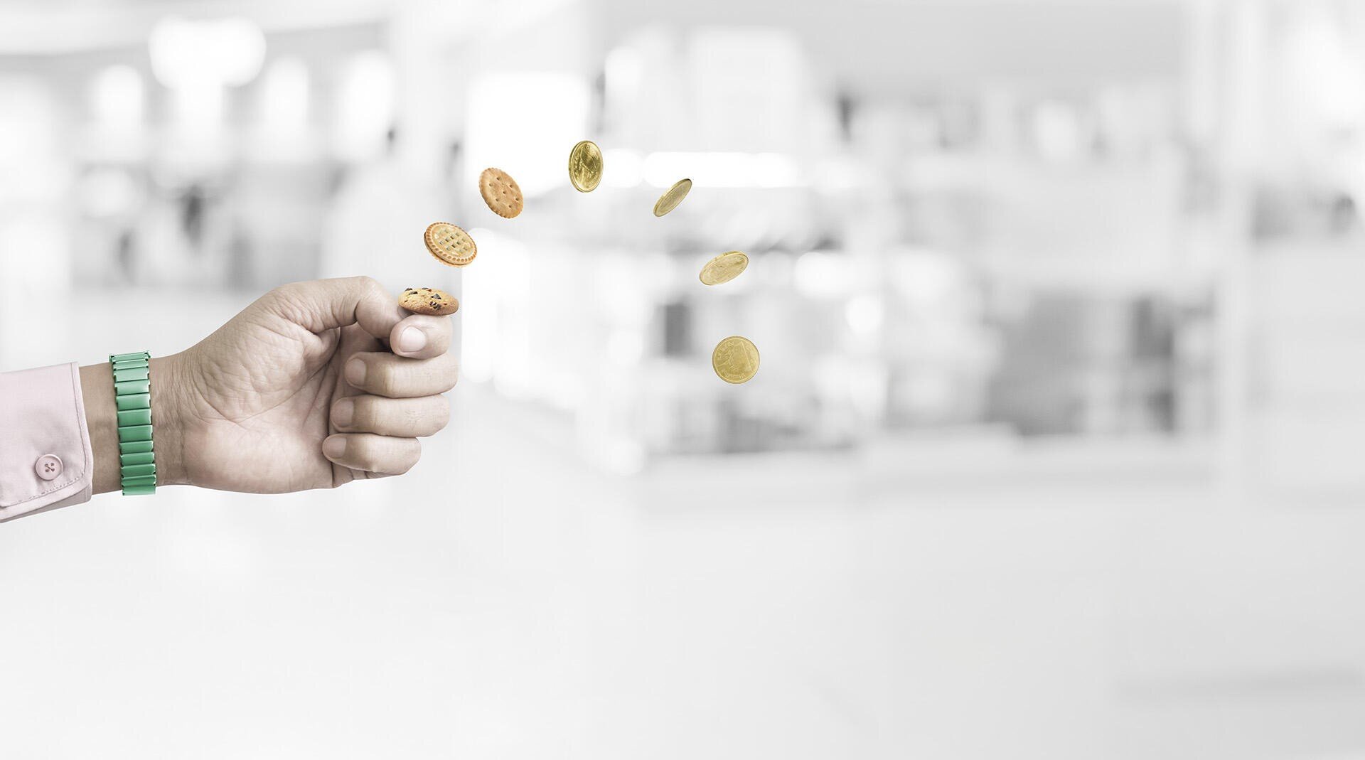 A hand wearing a green watch flicks several coins into the air, with a blurred, light-colored indoor background. The coins are mid-flight and appear to be the main focus of the image.