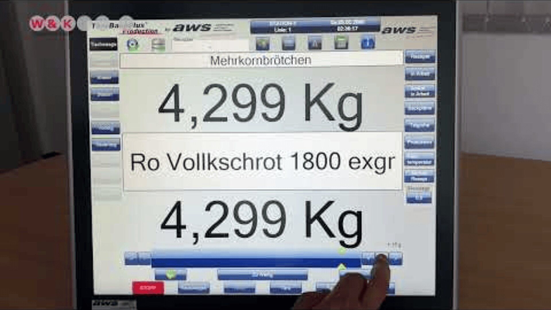 Ein Touchscreen mit einer Bäckerei-Schnittstelle zeigt das Gewicht 4,299 kg und den Text Mehrkornbrötchen und Ro Vollkschrot 1800 exgr. Eine Hand drückt eine Taste auf dem Bildschirm.