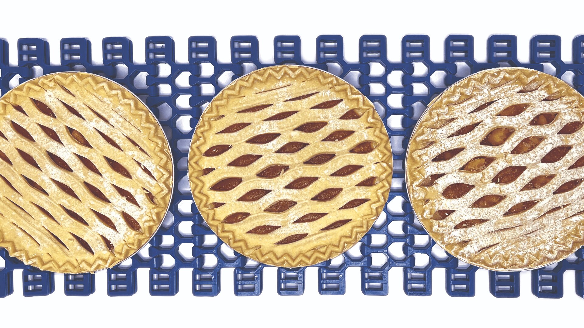 Three round lattice-top pies with golden crusts are placed in a row on a blue conveyor belt, viewed from above against a white background.