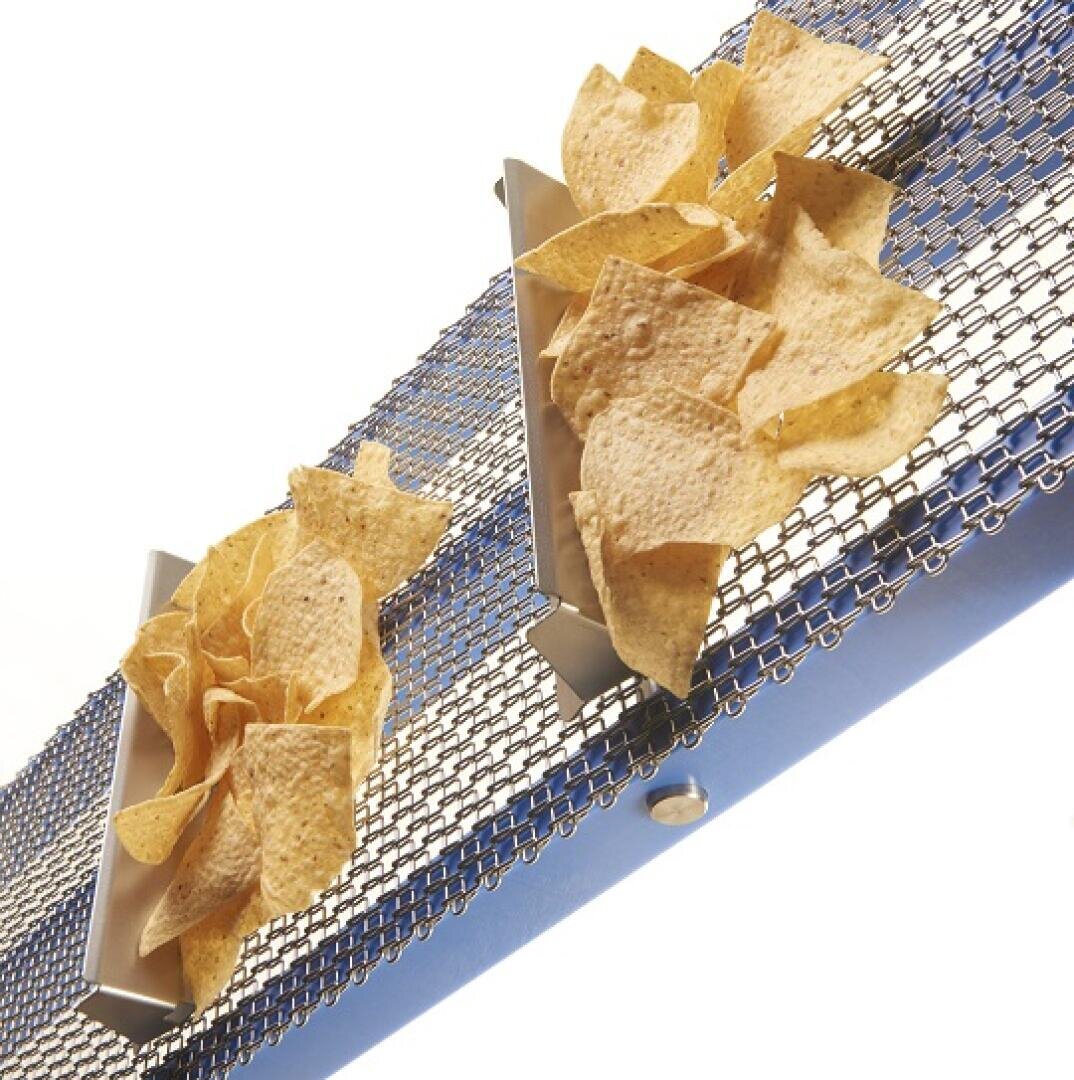 Tortilla chips moving on a metal conveyor belt, separated into two sections. The background is plain white.