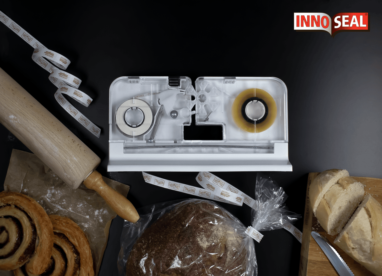 A tabletop bag sealing machine sits on a black surface surrounded by a rolling pin, pastries, a loaf of bread in a sealed bag, sliced bread, and a knife. INNO SEAL is displayed in the top right corner.