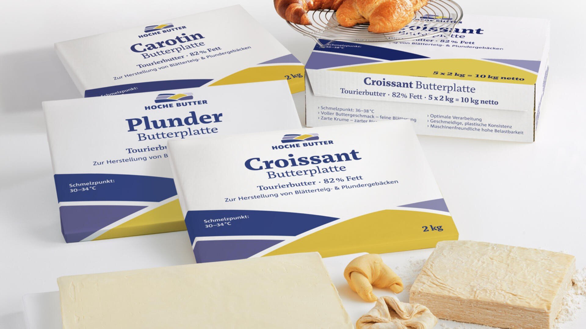 Butterblöcke, die für verschiedene Gebäckarten gekennzeichnet sind, werden neben Croissants und einem Stück Butter ausgestellt. Die Verpackungen sind meist weiß mit blauen und gelben Akzenten und deutschem Text.
