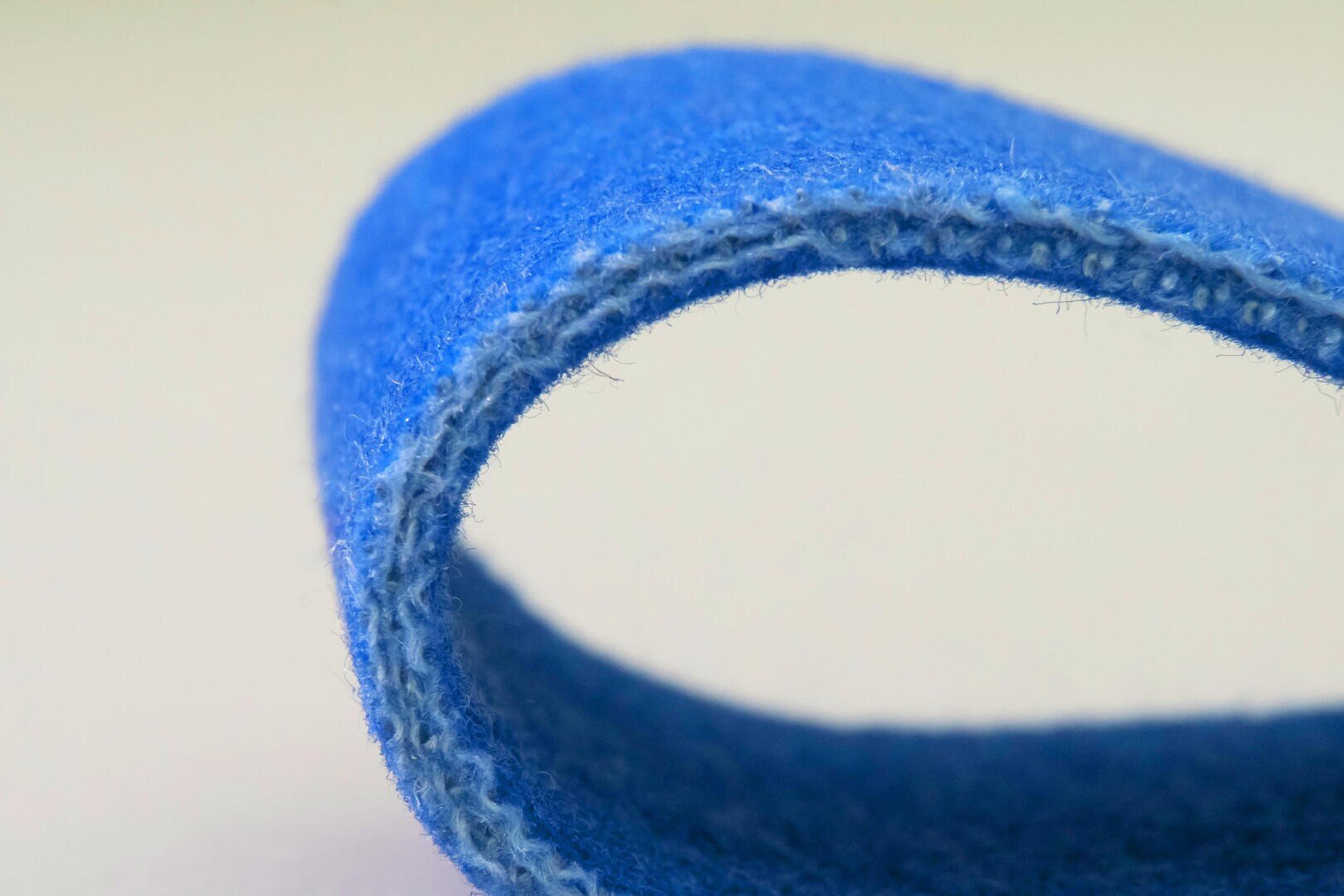 A close-up photo of a looped piece of blue felt fabric, showing its soft, fuzzy texture and stitched edge against a light, neutral background.