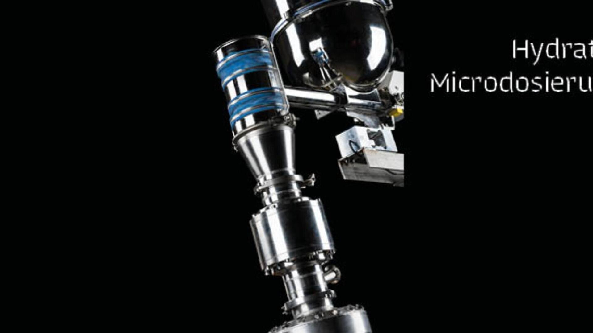 A close-up view of a metallic industrial machine with cylindrical components and blue accents, shown against a black background with partial white text on the right side.