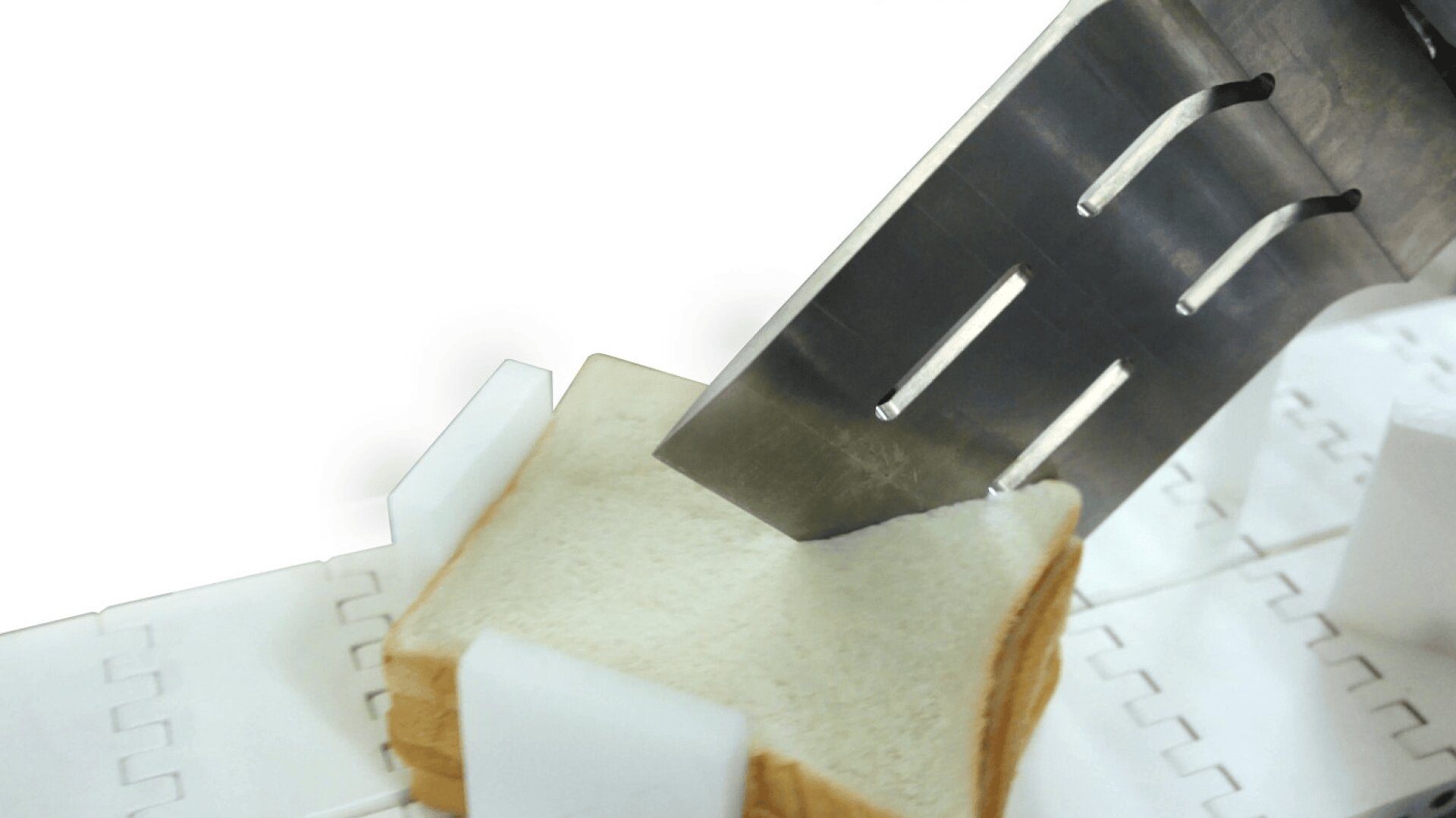 Nahaufnahme eines Brotschneidemessers, das einen Stapel von Weißbrotscheiben auf einem weißen Fördersystem durchschneidet.