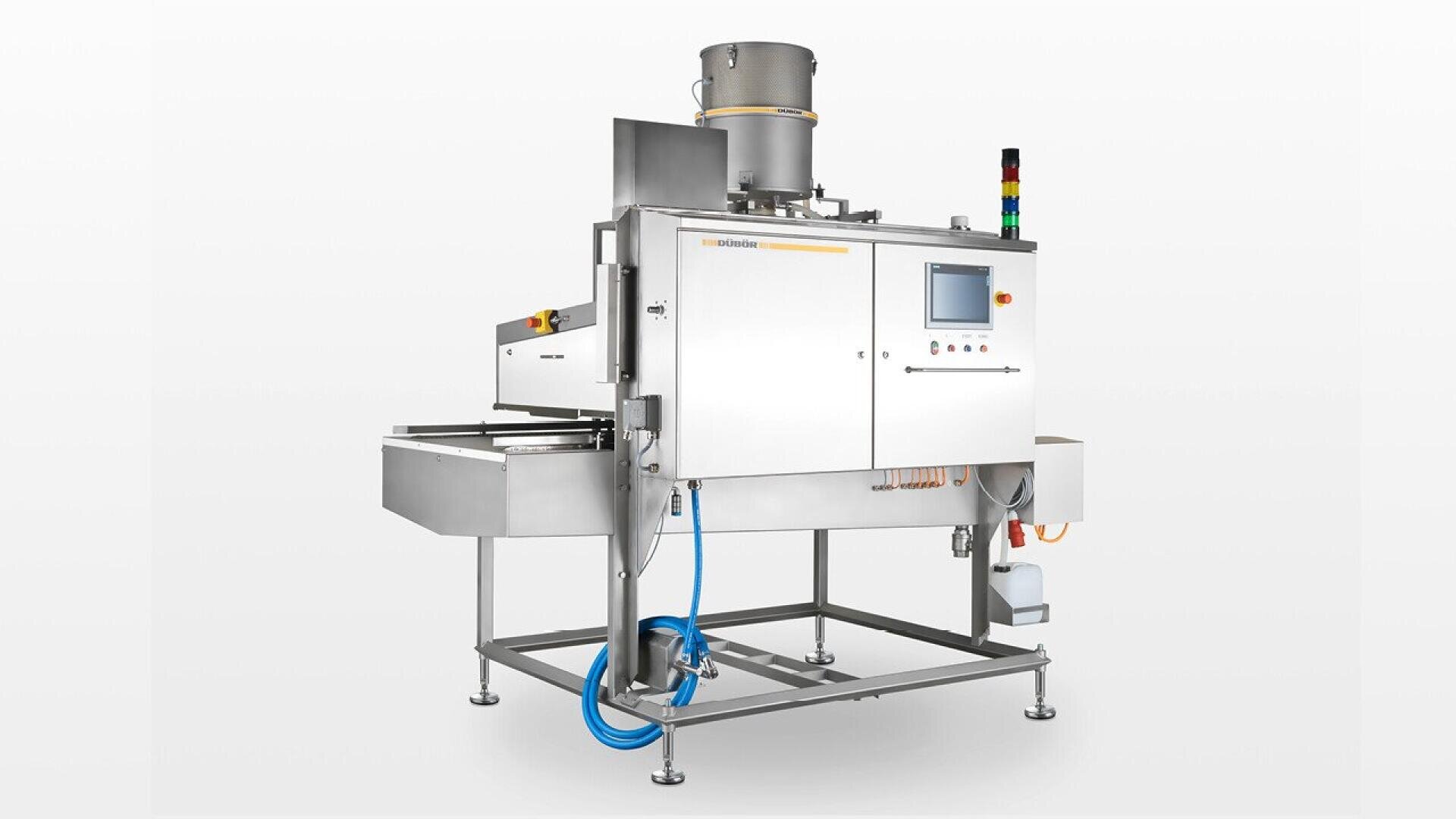 A stainless steel industrial food processing machine with a digital control panel, indicator lights, and various attachments, standing on metal legs with cables and hoses connected.