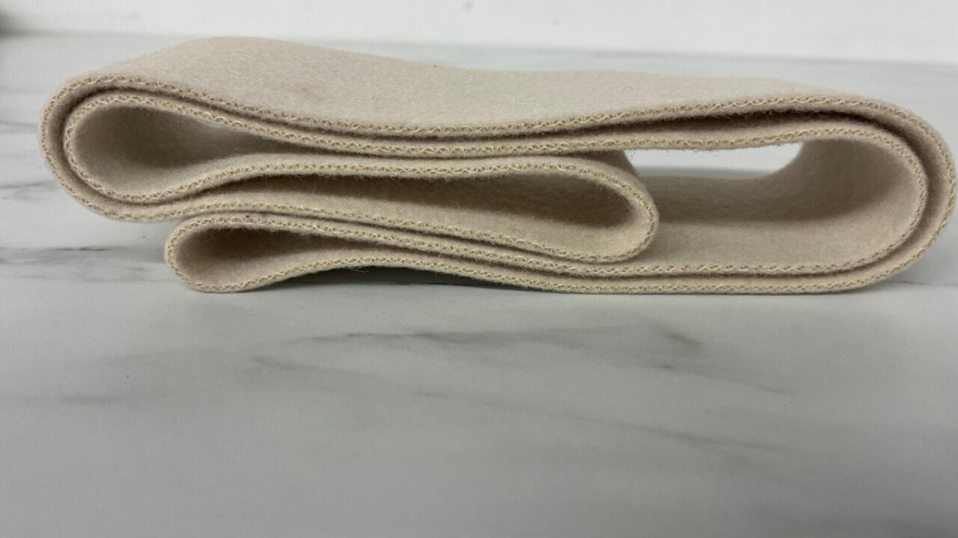 A beige, rectangular strip of fabric is neatly folded on a white marble surface, viewed from the side.