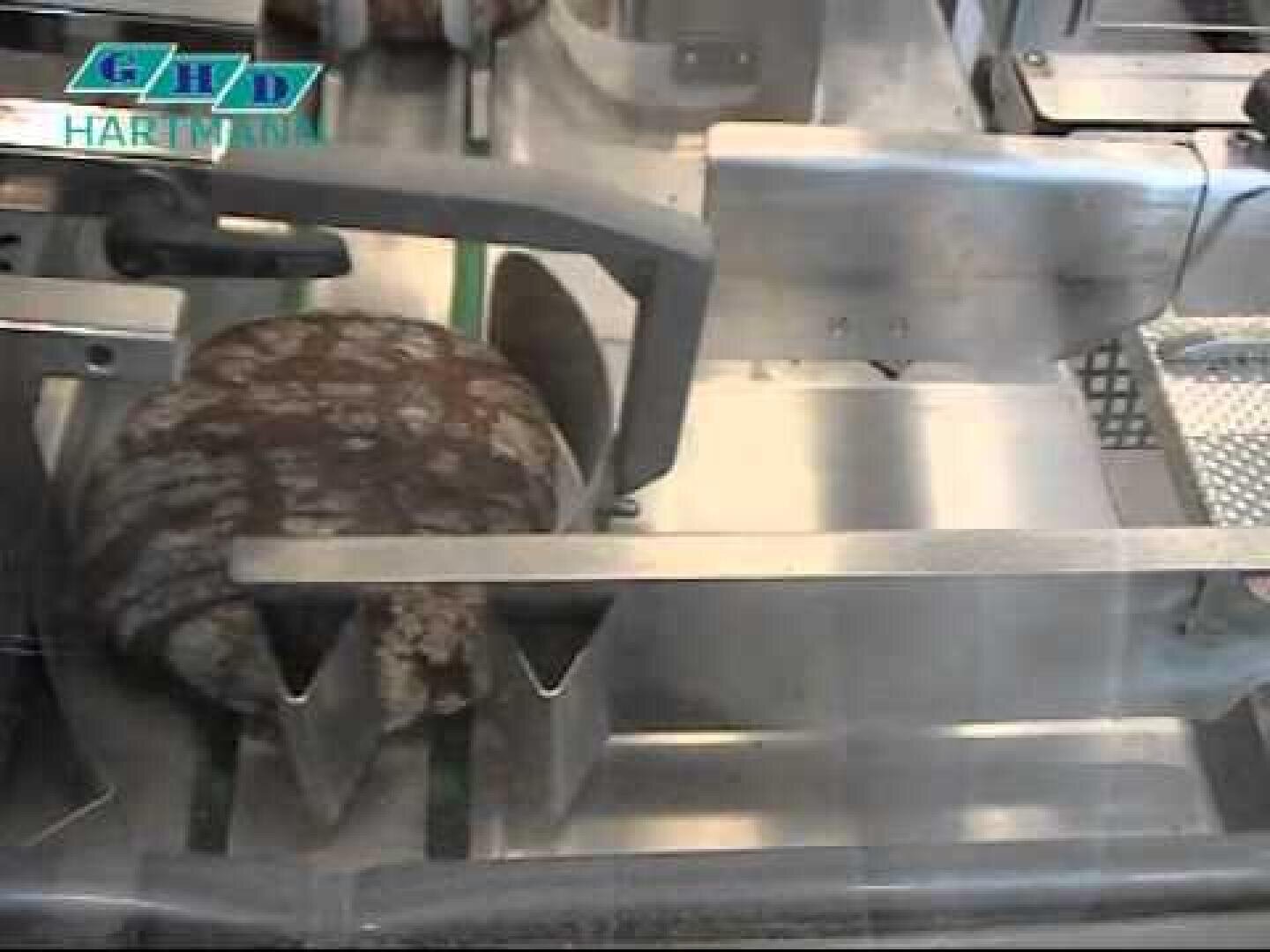 A sliced loaf of bread moves through a stainless steel industrial bread-slicing machine, with the GHD Hartmann logo visible in the upper left corner.