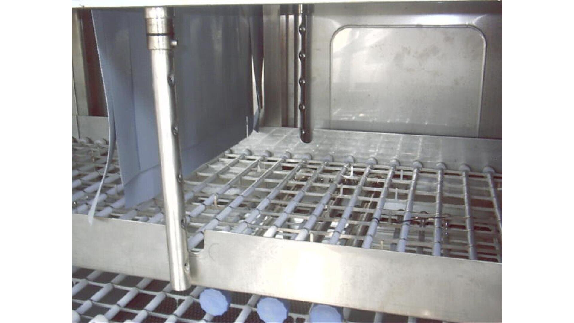 Nahaufnahme des Inneren einer gewerblichen Geschirrspülmaschine. Zu sehen sind Metallkörbe, Sprüharme und Teile des Spülmechanismus in einem Edelstahlgehäuse.