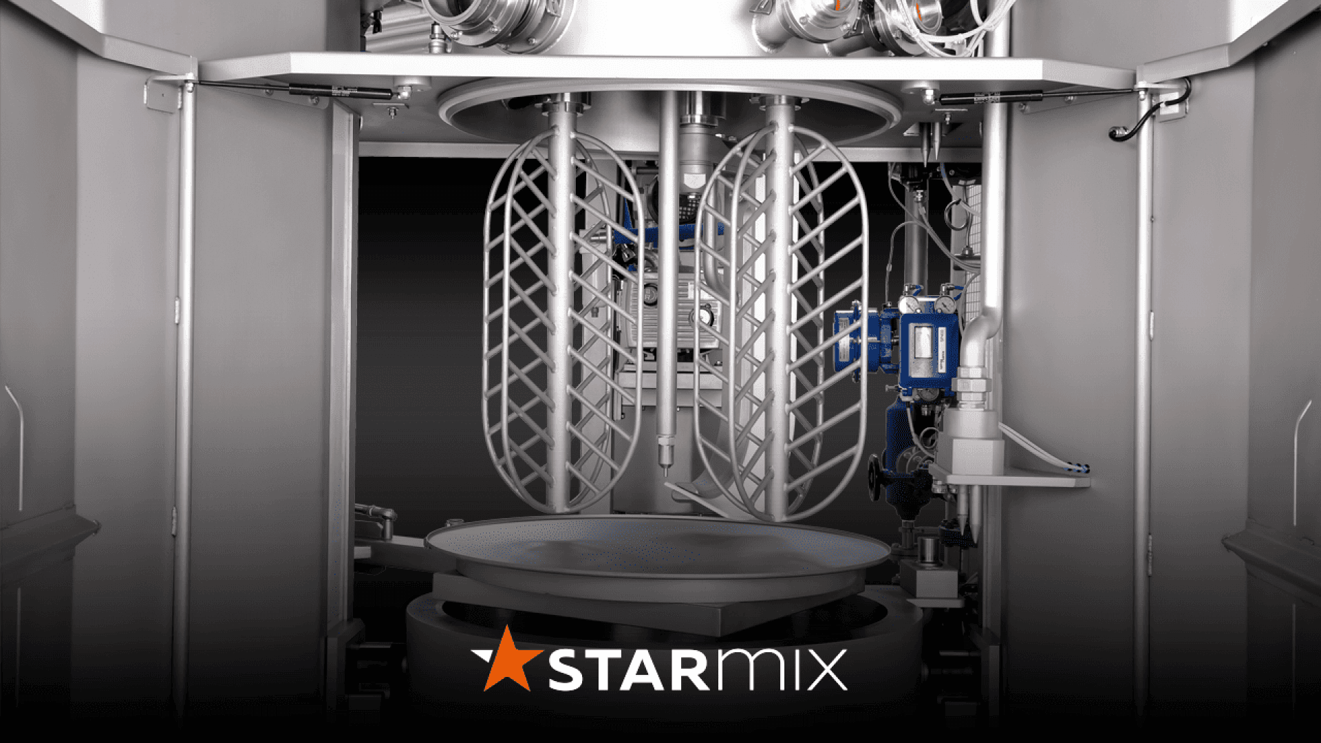 Close-up view of a large industrial mixer with two spiral mixing arms and a circular mixing platform. The machine is metallic and labeled STARMIX at the bottom with an orange star-shaped logo.