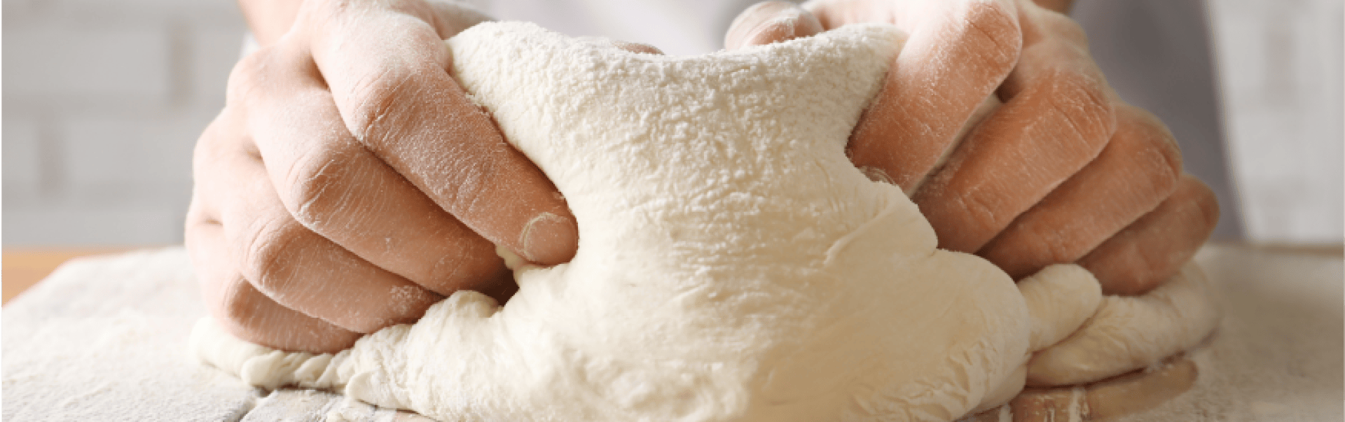Close-up of hands kneading a soft ball of dough dusted with flour on a wooden surface to prepare it for baking.