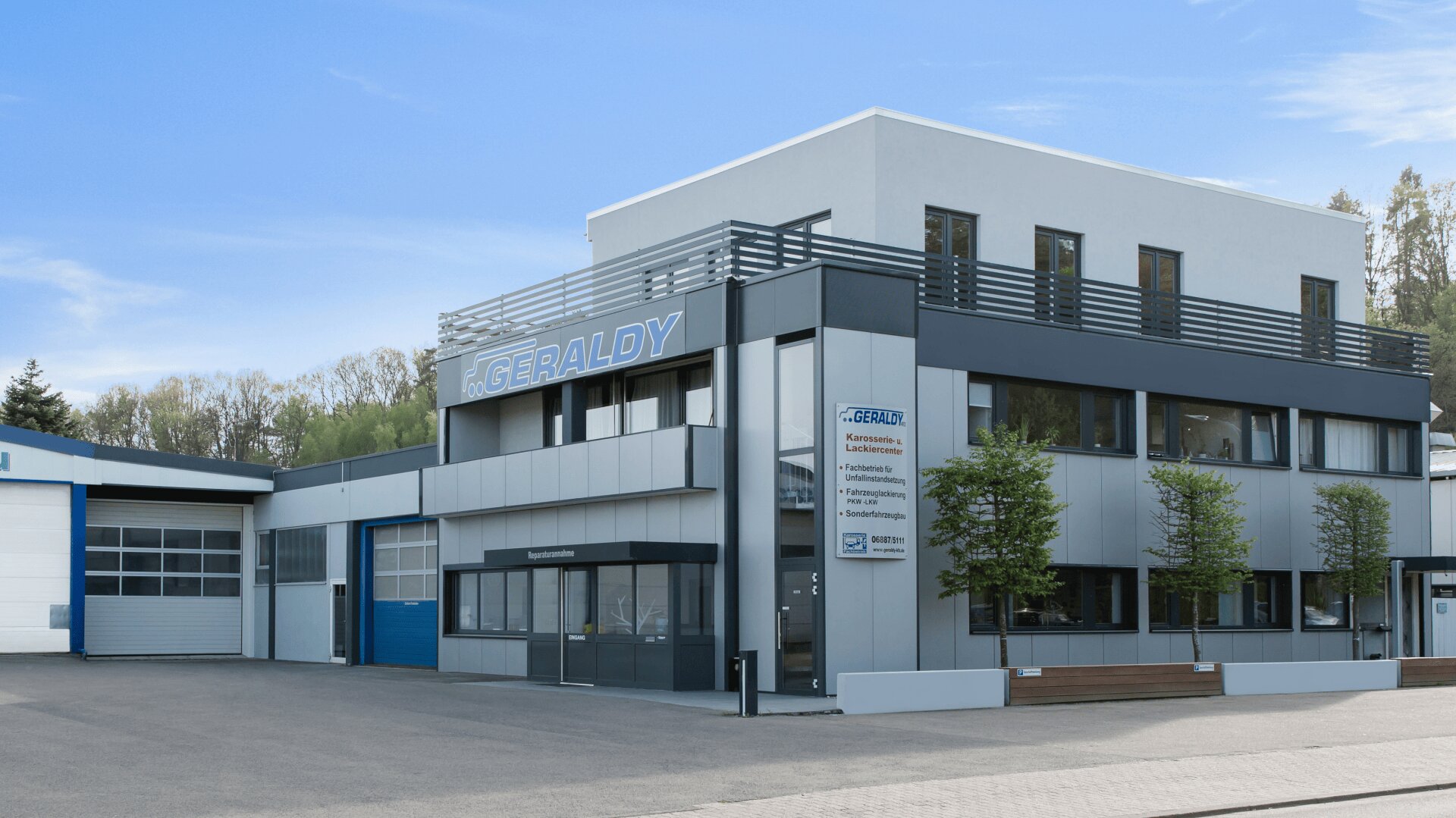 Ein modernes, grau-weißes Geschäftsgebäude mit großen Fenstern, das die Aufschrift GERALDY trägt, steht unter einem klaren blauen Himmel. Auf der Vorderseite stehen Bäume, ein Schild mit der Auflistung der Dienstleistungen und ein blaues Garagentor.