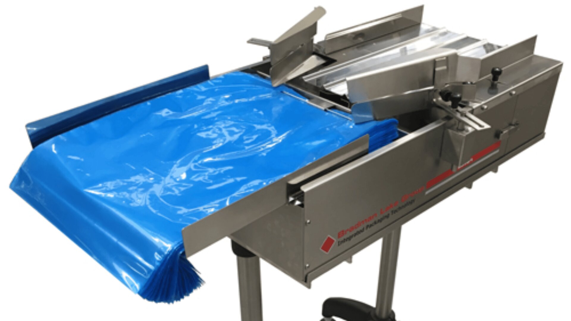 A stainless steel automated packaging machine with a roll of blue plastic film loaded and ready for sealing or wrapping products. The machine stands on metal legs and has adjustable components.