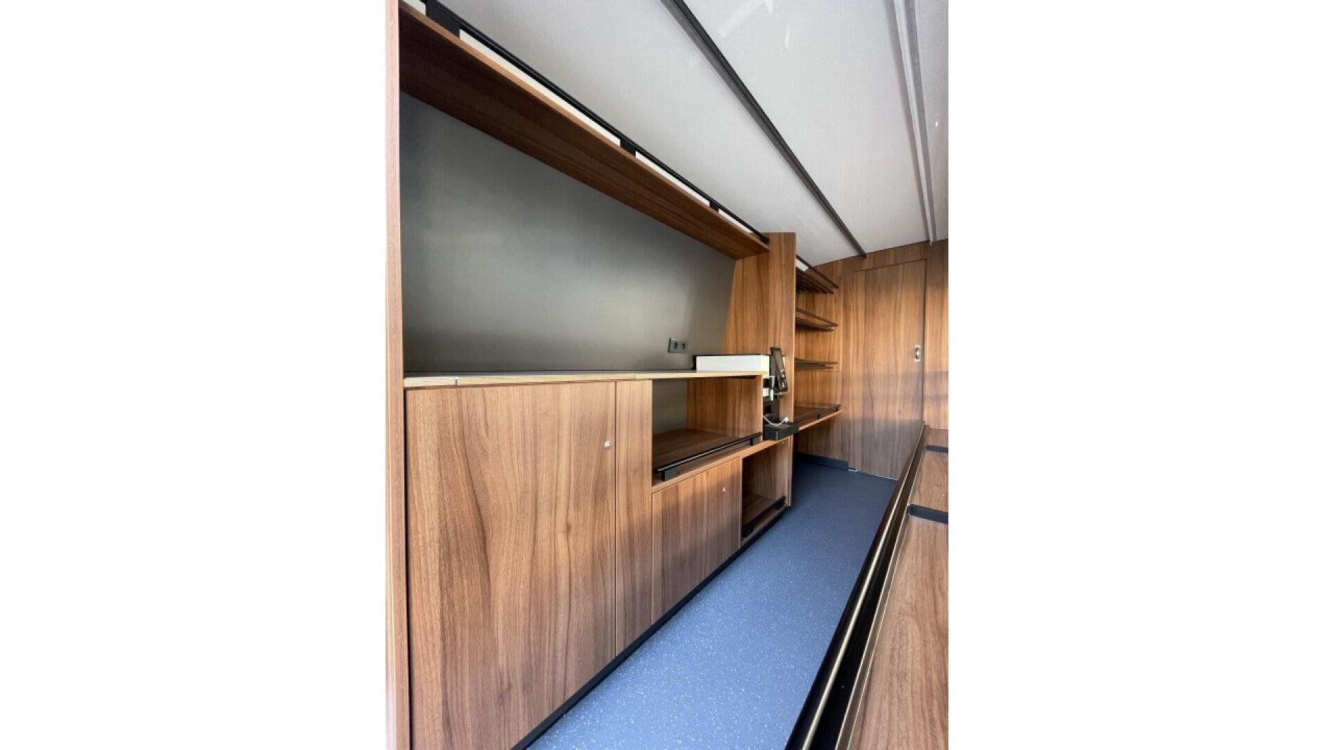 A modern, minimalist kitchen with wood cabinets, open shelves, and a dark countertop. The design features clean lines, a built-in coffee maker, and a sleek, uncluttered appearance.