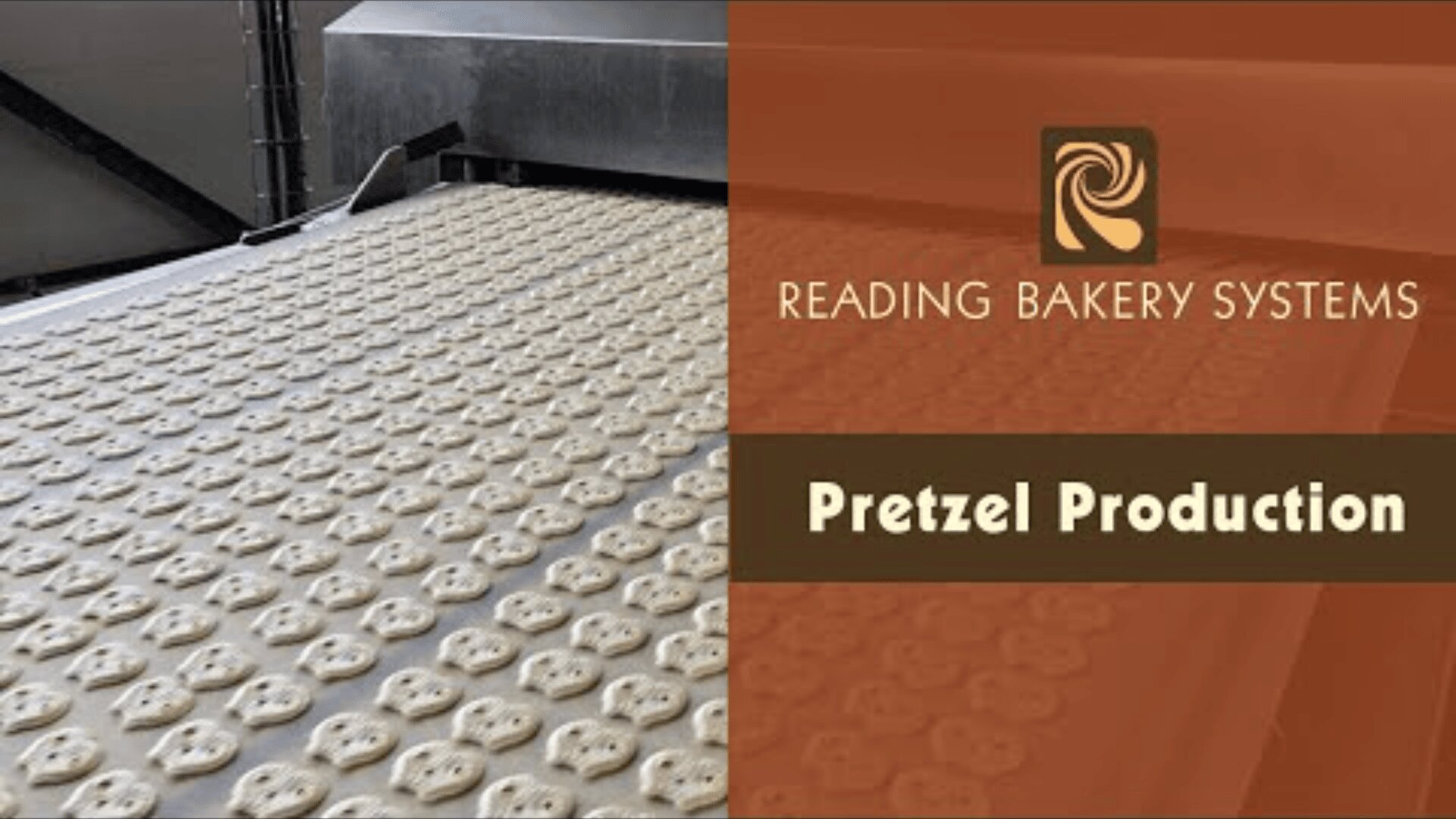 Rows of raw pretzels on a conveyor belt in a factory, with the Reading Bakery Systems logo and the words Pretzel Production on a brown board on the right.