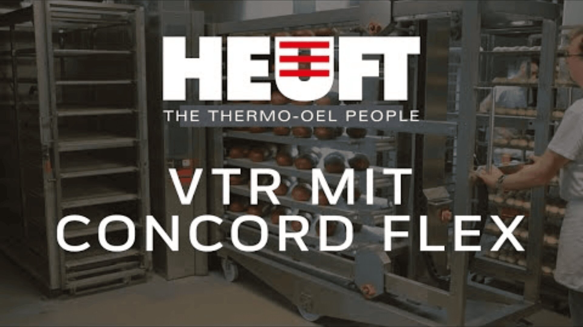 Eine Person bewegt ein Regal mit Backwaren in einer Großküche. Der überlagerte Text lautet: HEUFT THE THERMO-OEL PEOPLE VTR MIT CONCORD FLEX. Im Hintergrund sind Metallgestelle und Tabletts zu sehen.
