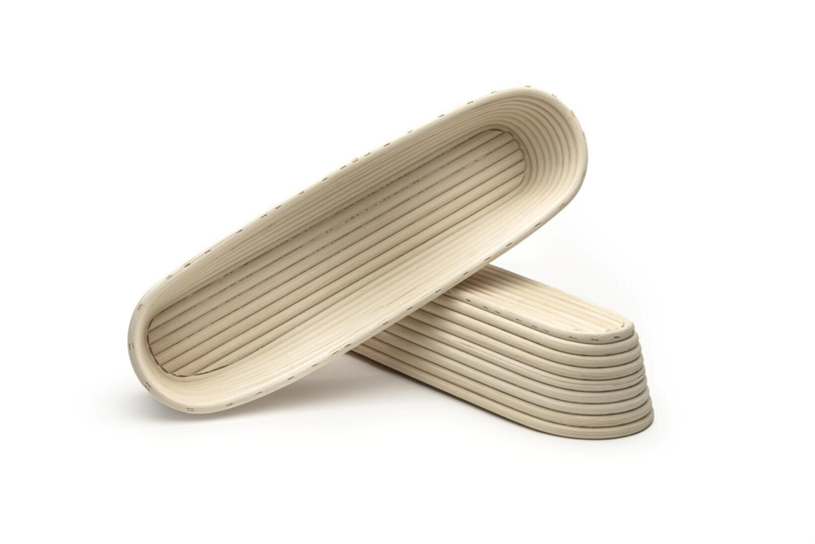 Zwei längliche, ovale Gärkörbe aus Weidengeflecht sind kreuz und quer auf einem weißen Hintergrund gestapelt. Die Körbe haben geriffelte Seiten und werden zum Gären von Brotteig verwendet.