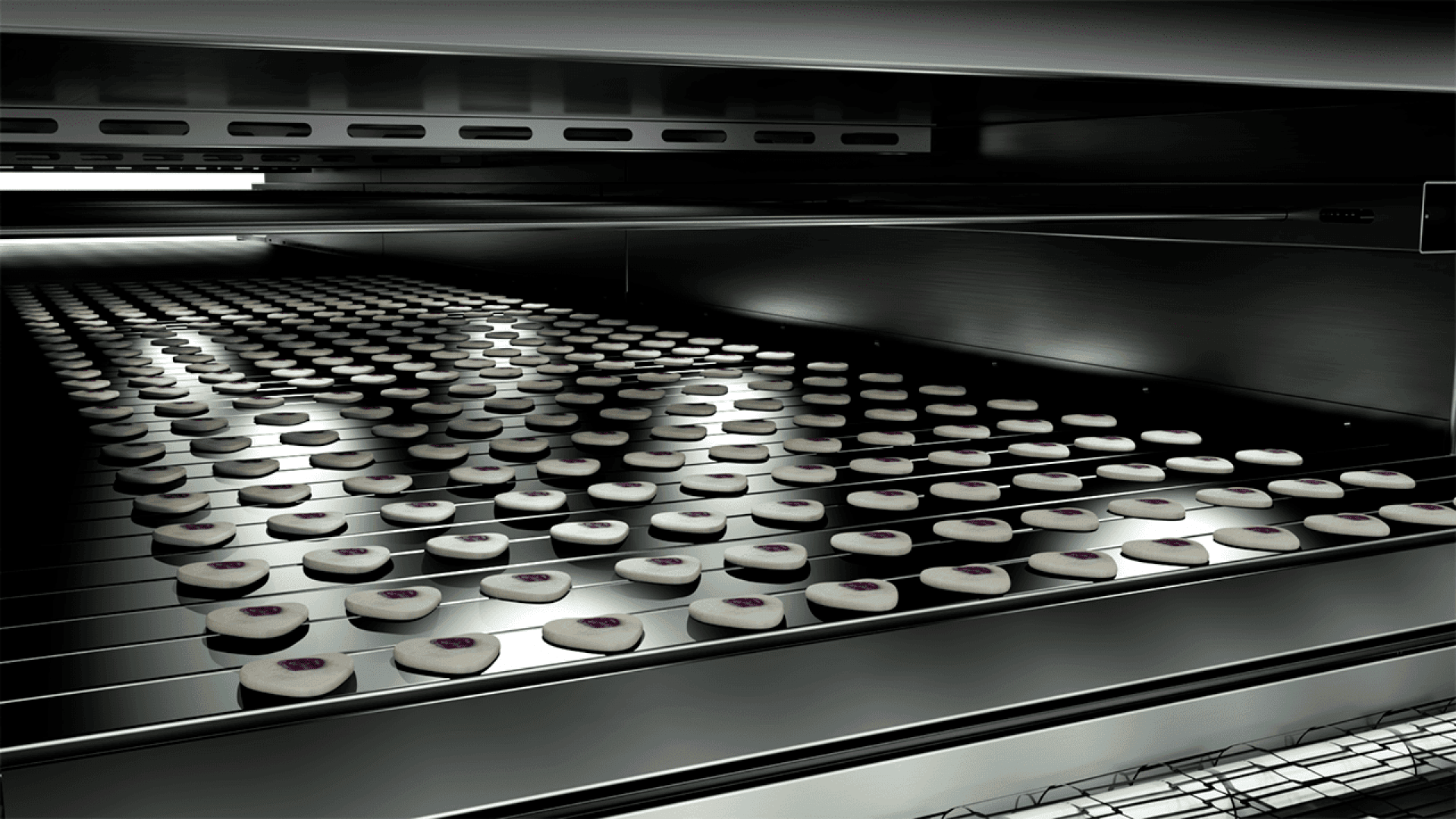 Reihen von runden Keksen mit einem Klecks Marmelade in der Mitte laufen auf einem Fließband durch einen großen Industrieofen, was auf eine Massenproduktion in einer Großbäckerei schließen lässt.