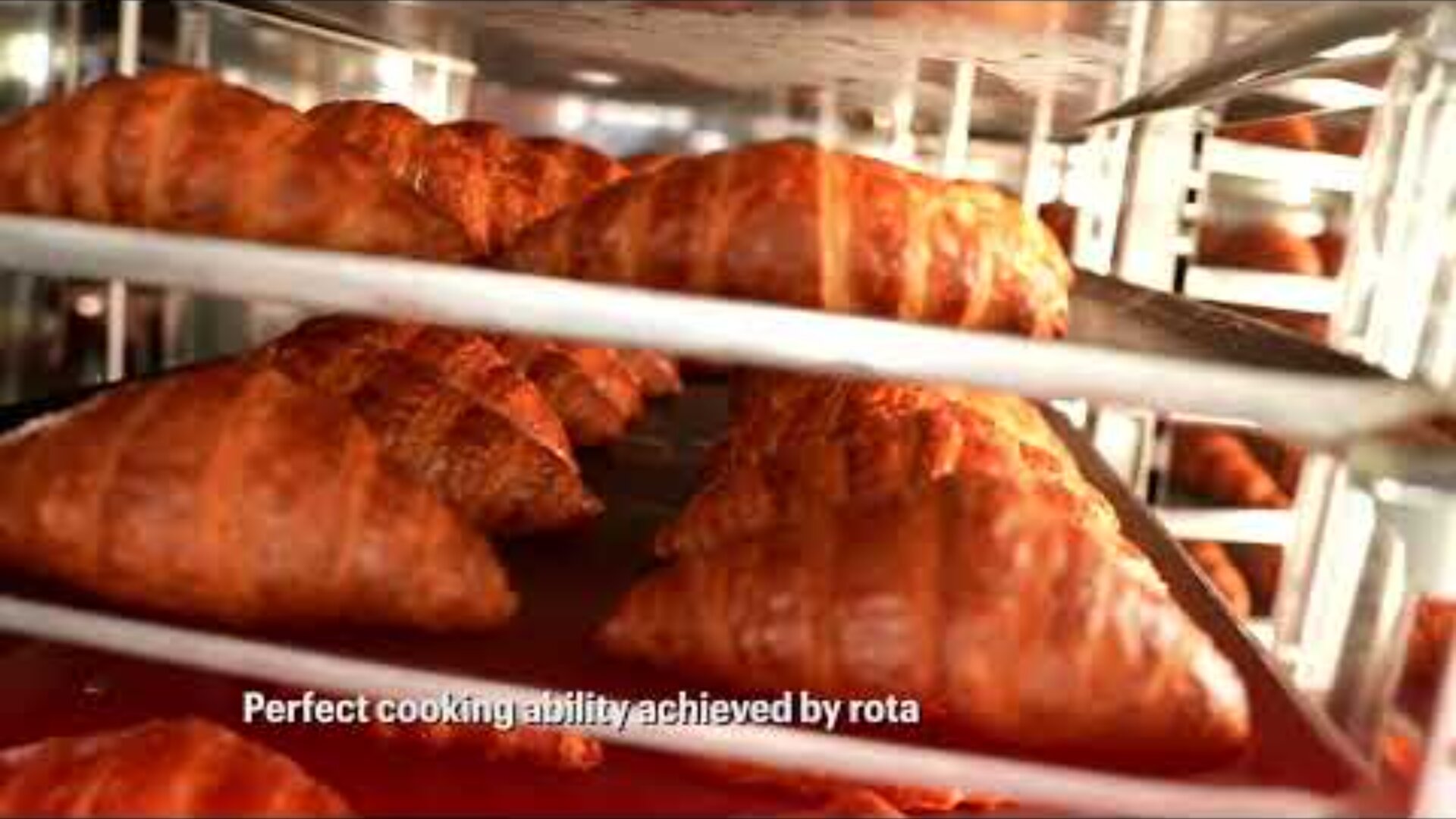 Golden brown croissants baking on metal trays inside an oven, with the text Perfect cooking ability achieved by rota partially visible at the bottom of the image.