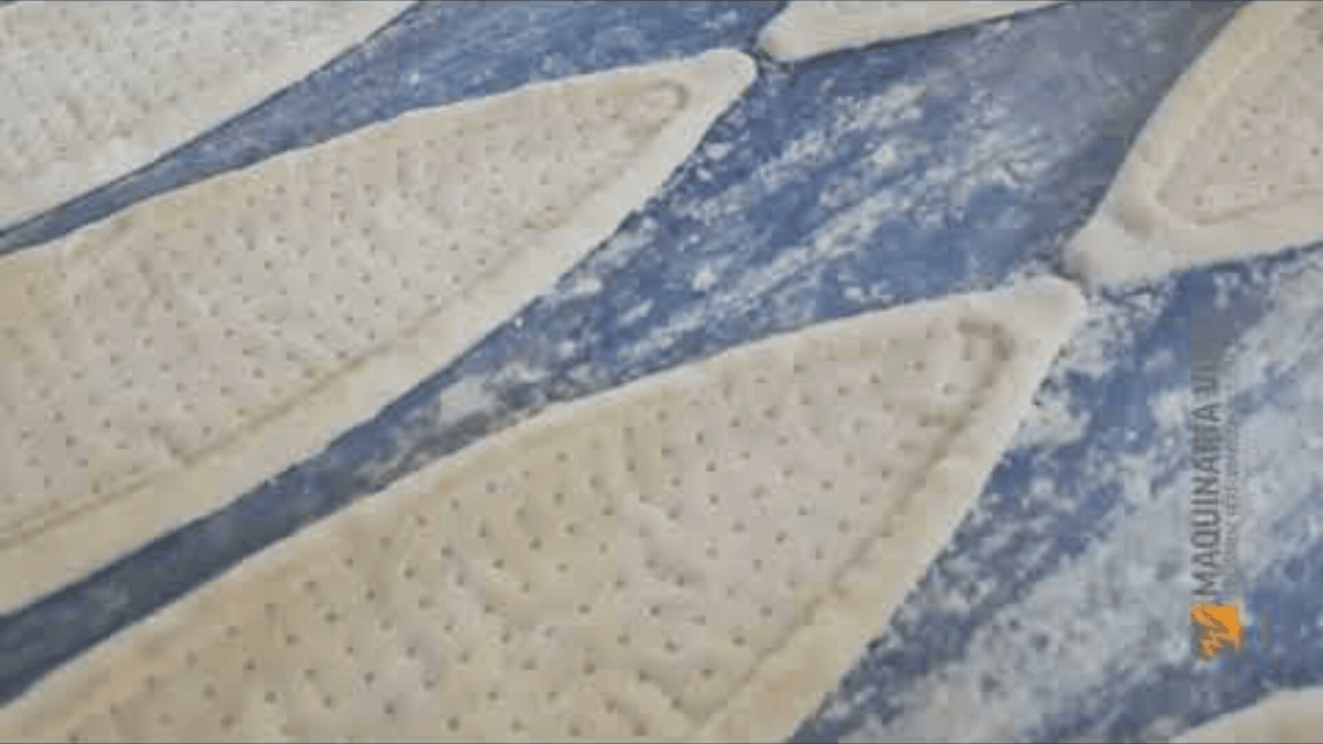 Nahaufnahme mehrerer roher, ovaler Teigstücke mit gelochter Oberfläche auf einer bemehlten blauen Arbeitsfläche, bereit zum Backen.