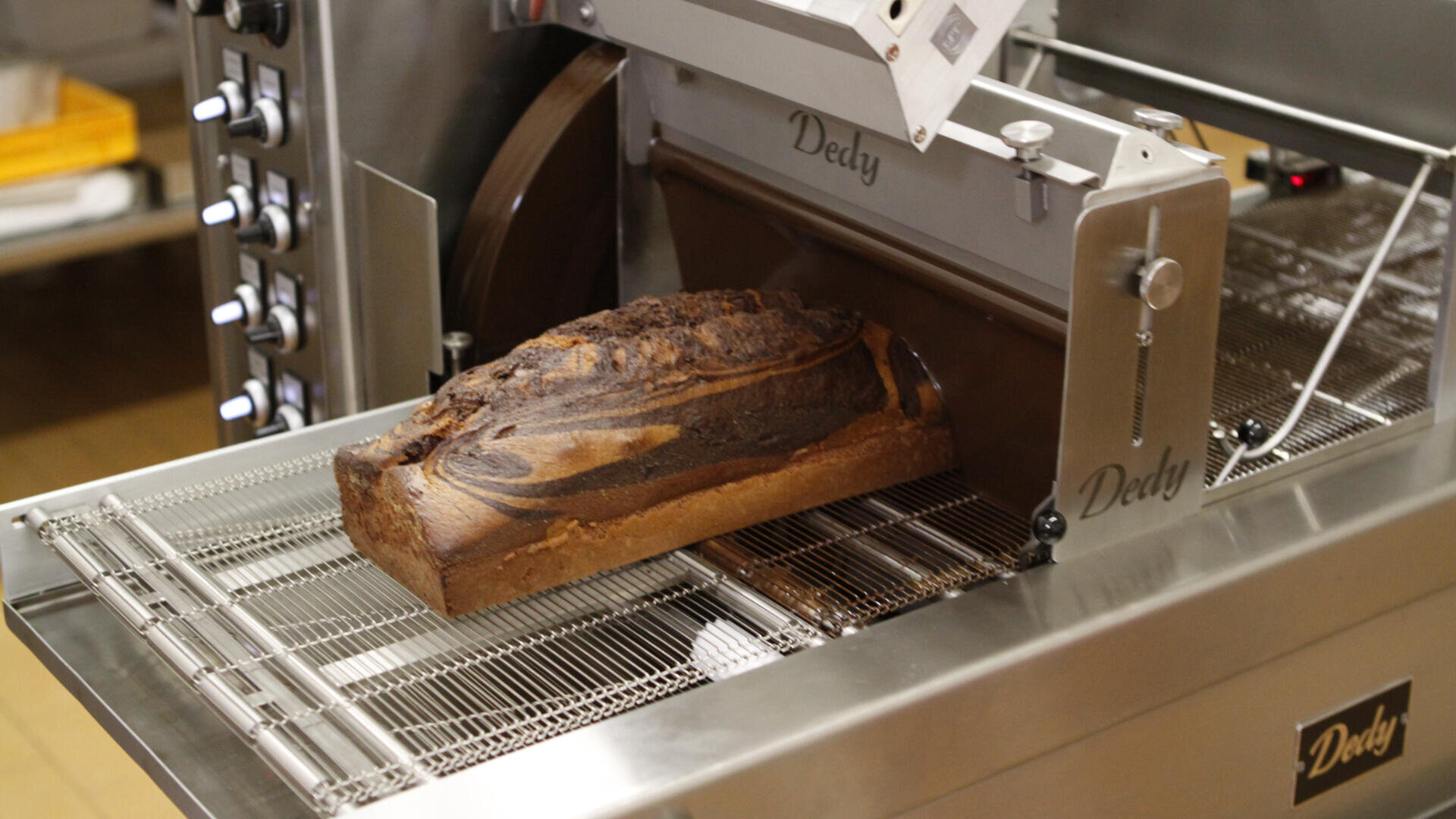 Ein Laib marmoriertes Brot wird von einer handelsüblichen Brotschneidemaschine in einer Bäckerei in Scheiben geschnitten.