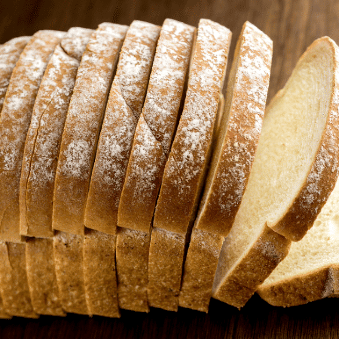 A close-up of a loaf of sliced white bread with a dusting of flour on top, arranged on a wooden surface.