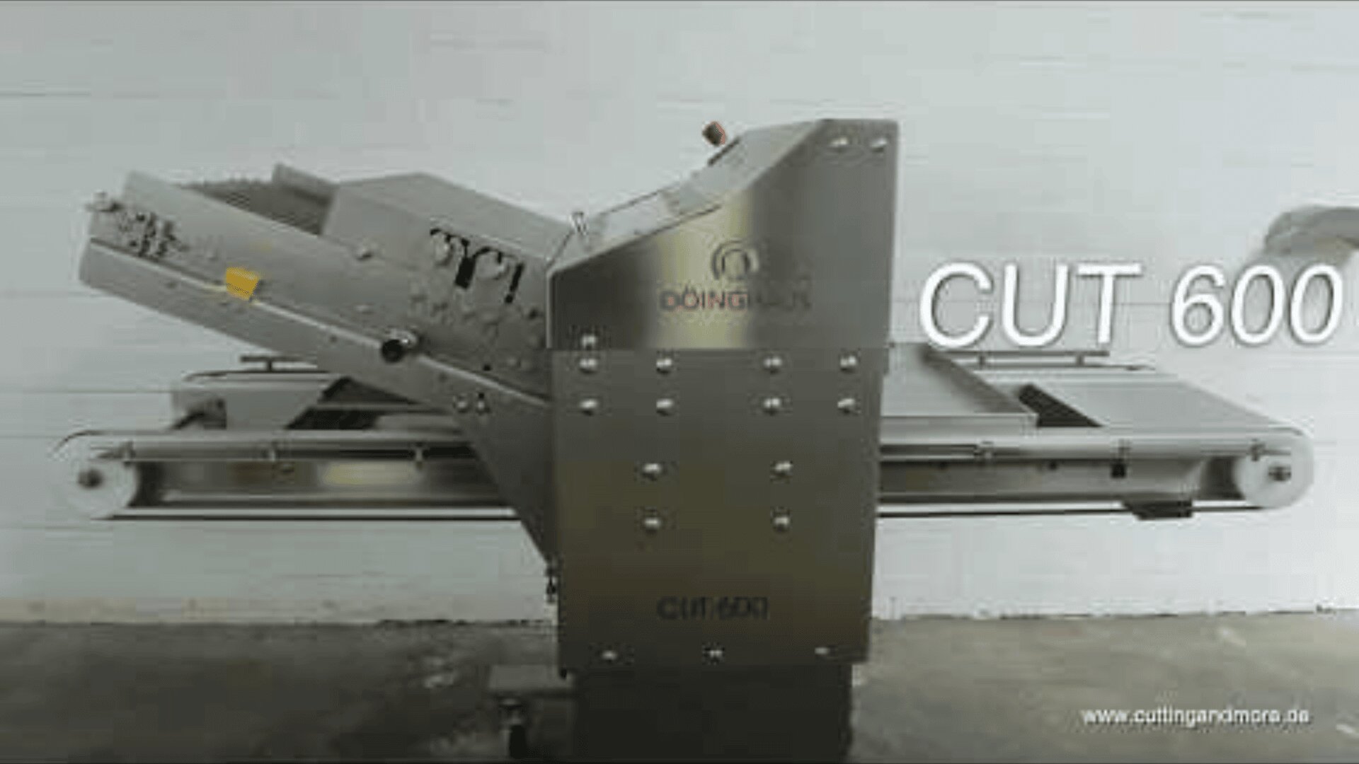 Eine industrielle Schneidemaschine aus rostfreiem Stahl mit der Bezeichnung CUT 600 ist vor einer schlichten weißen Wand abgebildet, wobei Förderbänder und Bedienelemente sichtbar sind. Das Logo und die Website des Herstellers sind ebenfalls auf der Maschine und dem Bild zu sehen.