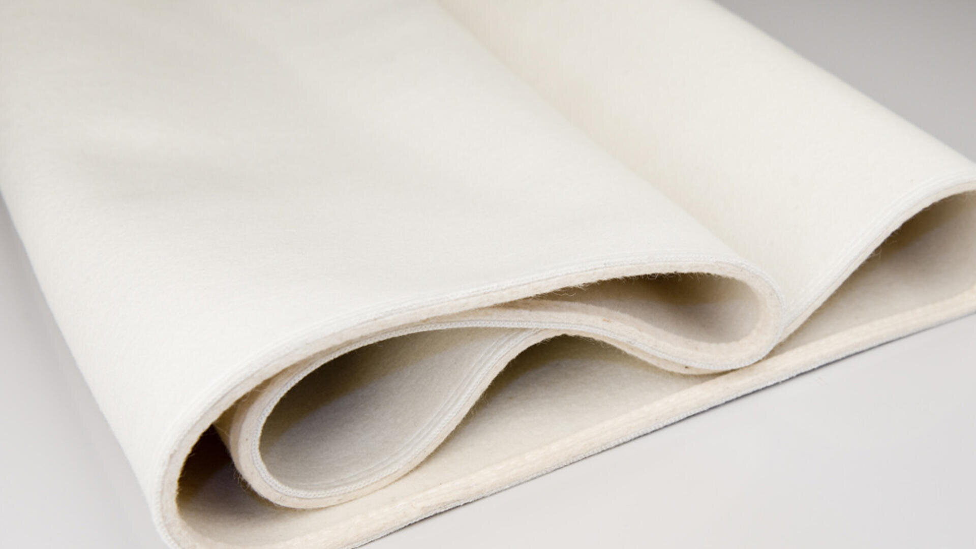 Eine Nahaufnahme eines dicken, gefalteten Stücks weichen, weißen Filzstoffs auf einer hellen Fläche.