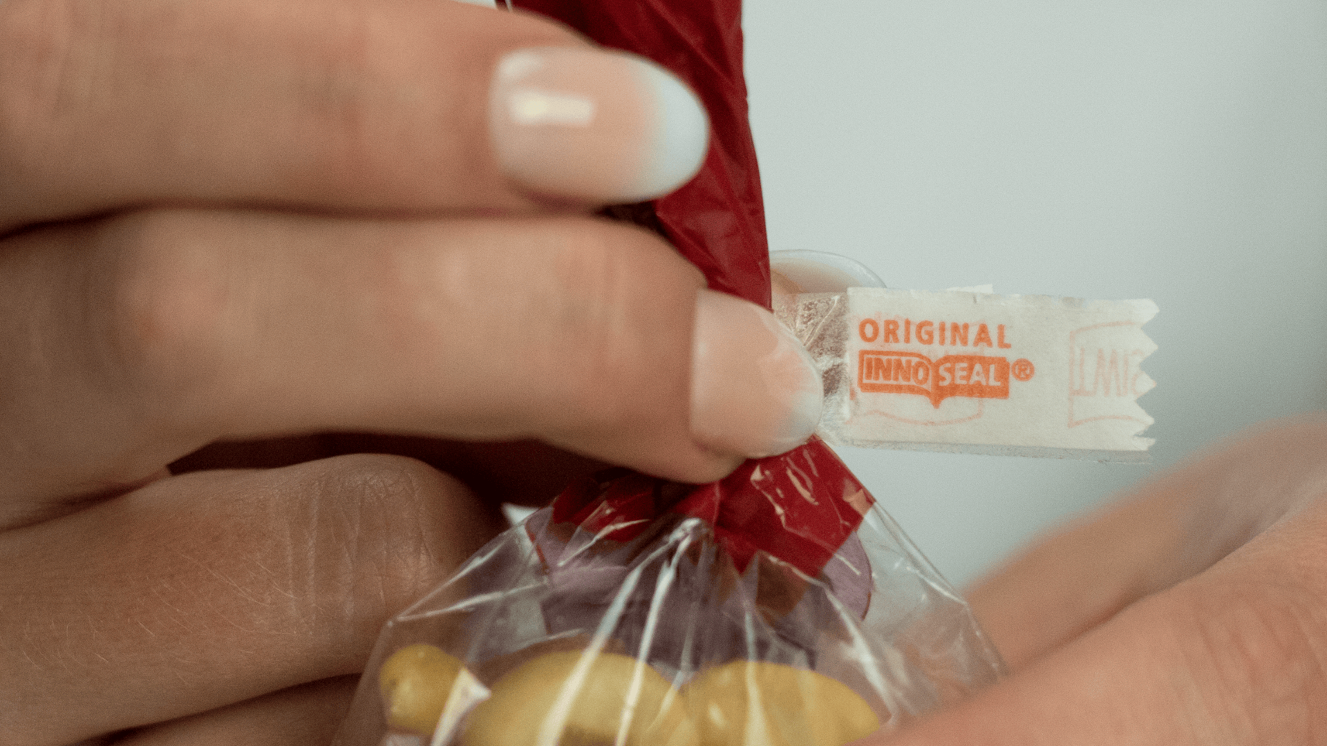 A close-up of hands sealing a plastic bag with a red twist tie, showing a white label that reads ORIGINAL INNOSEAL. Yellow items are visible inside the bag.