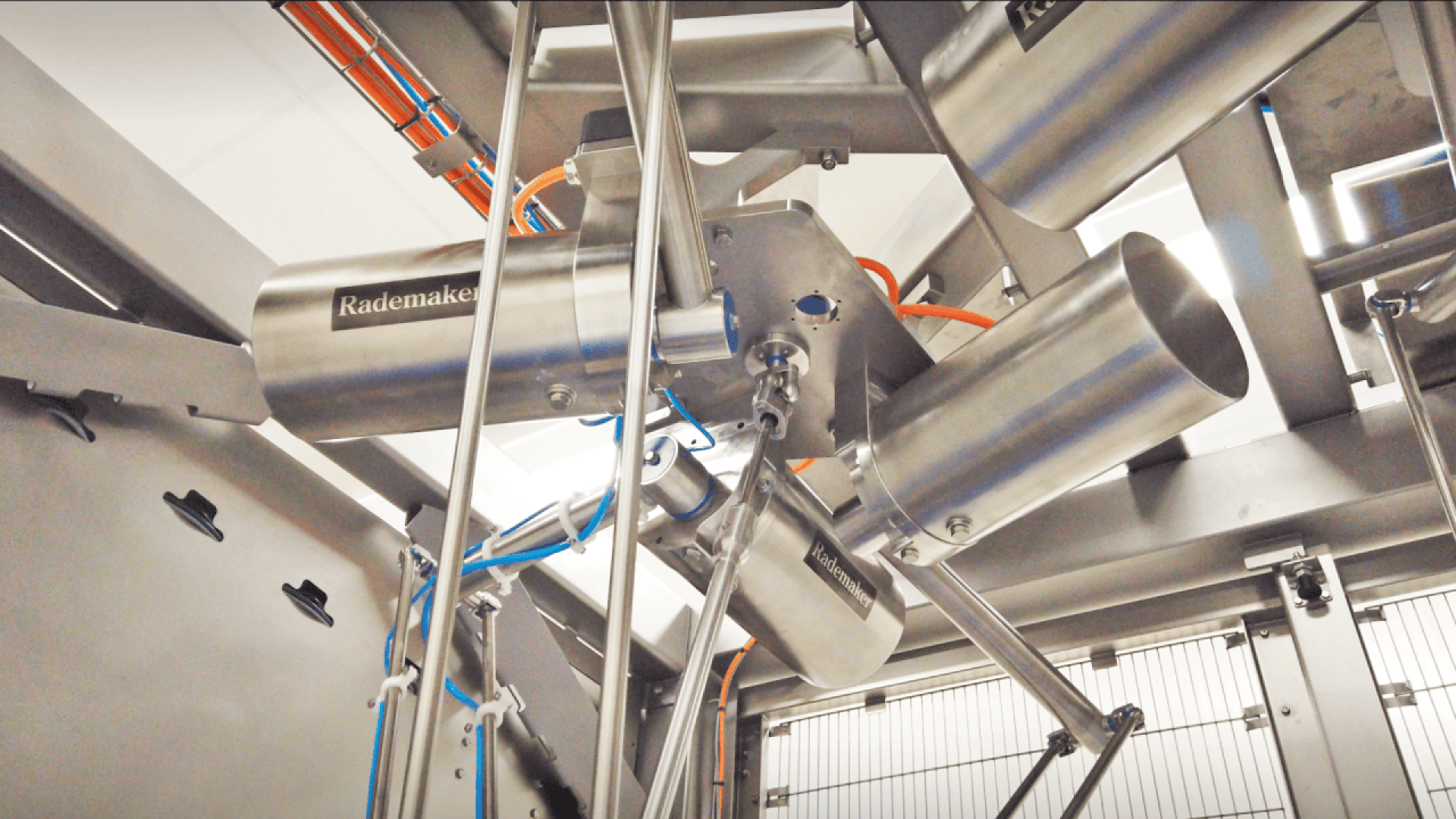 Nahaufnahme von Industriemaschinen aus rostfreiem Stahl mit dem Markenzeichen von Rademaker, mit zylindrischen Bauteilen, verschiedenen Kabeln und Metallrahmen in einer Fabrikumgebung.