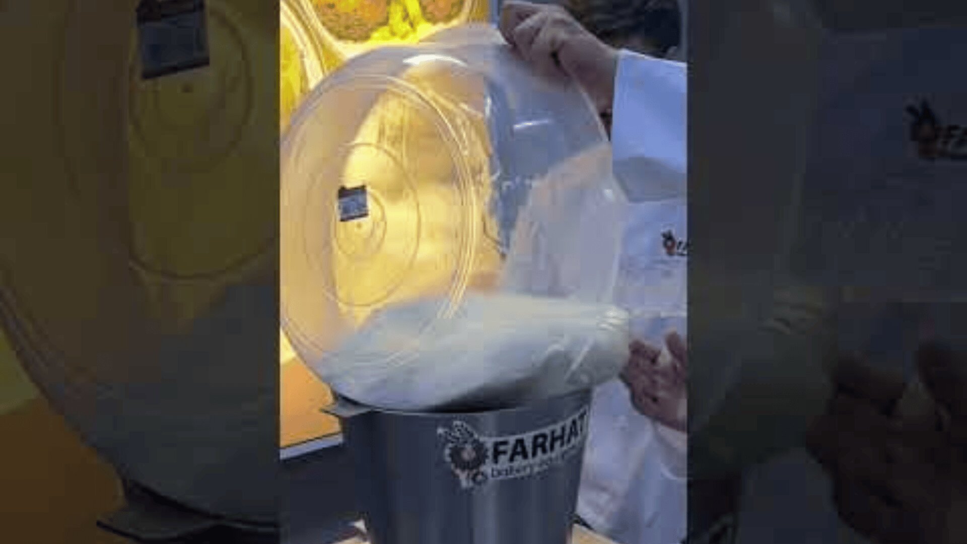 A person in a white lab coat pours a large container of white powder into a FARHAN industrial mixer in a workroom.