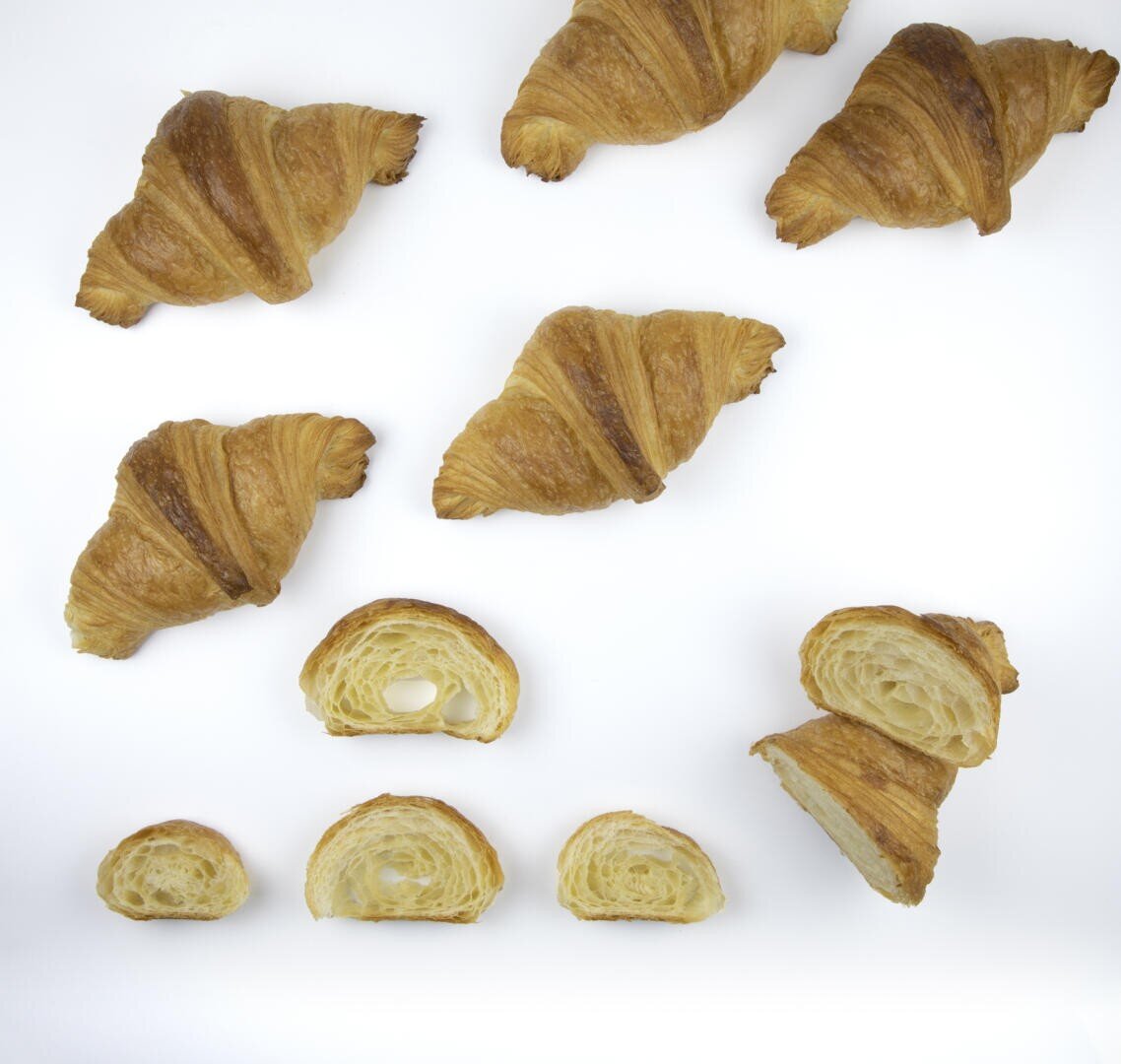 Eine Gruppe von ganzen und halbierten Croissants ist auf einem weißen Hintergrund angeordnet und zeigt ihre flockige, geschichtete innere Textur.
