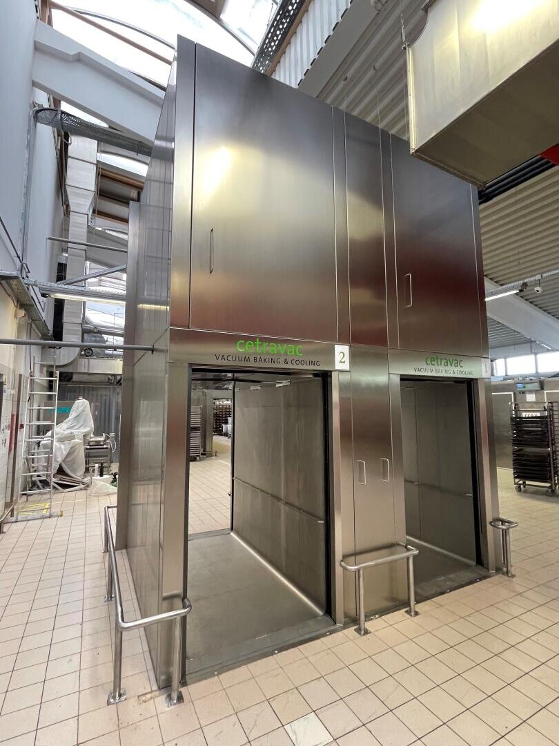 Large stainless steel vacuum baking and cooling chamber in a commercial kitchen or industrial facility, labeled Cetravac, with tiled floor, high ceiling, and metal railings around the unit.