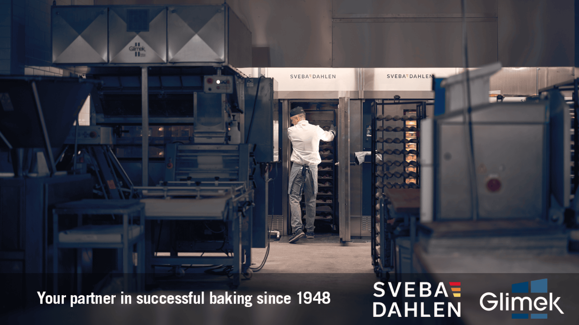 Ein Bäcker holt in einer Großbäckerei Brotkörbe aus Industrieöfen. Das Bild zeigt die Logos von Sveba Dahlen und Glimek mit dem Text „Ihr Partner für erfolgreiches Backen seit 1948“.